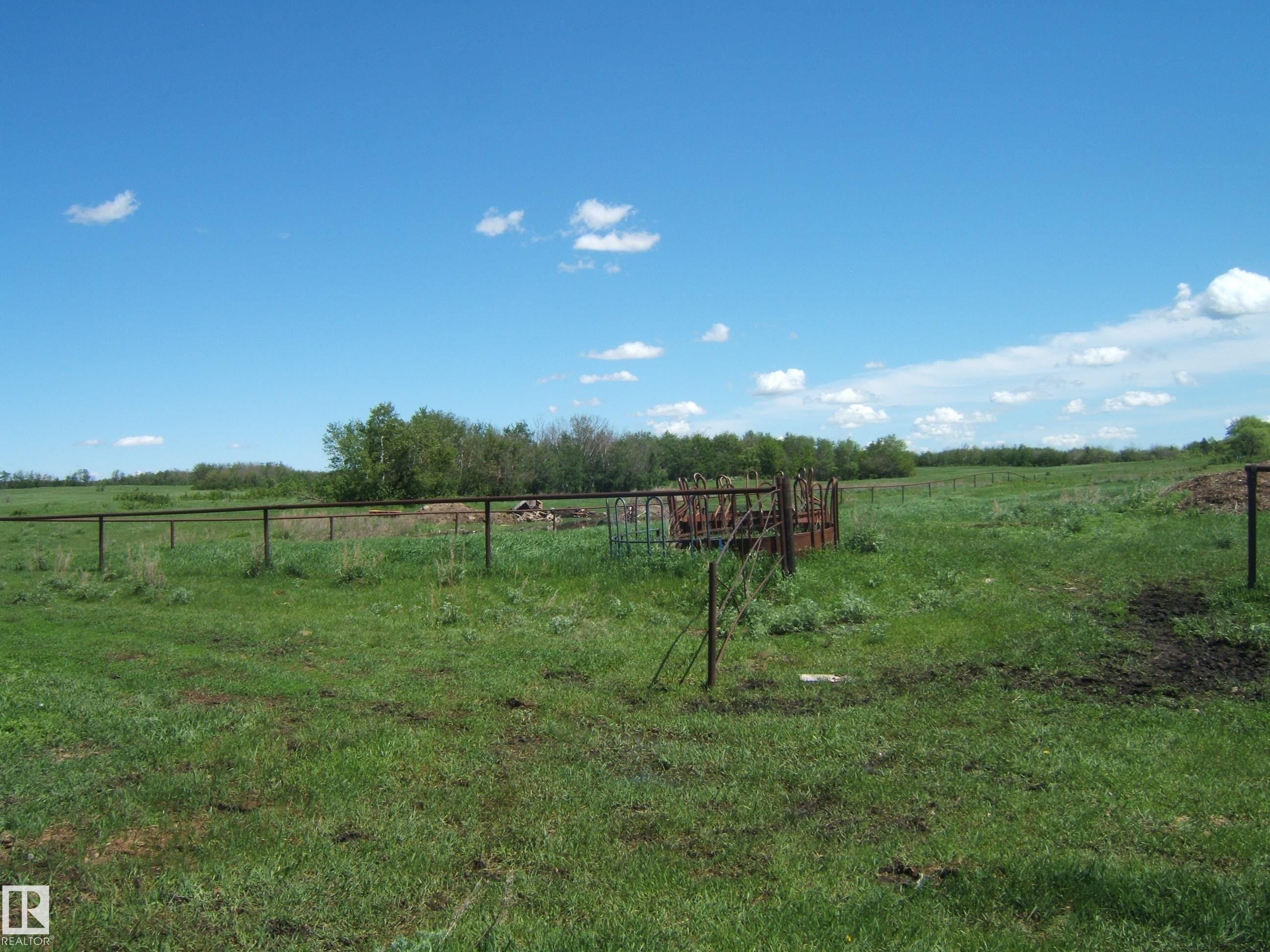 Expansive green pastureland featuring perimeter fencing, an enclosed feeding area, and a distant tree line defining the property's edge - 123064 Hwy 45, Rural Two Hills County, AB