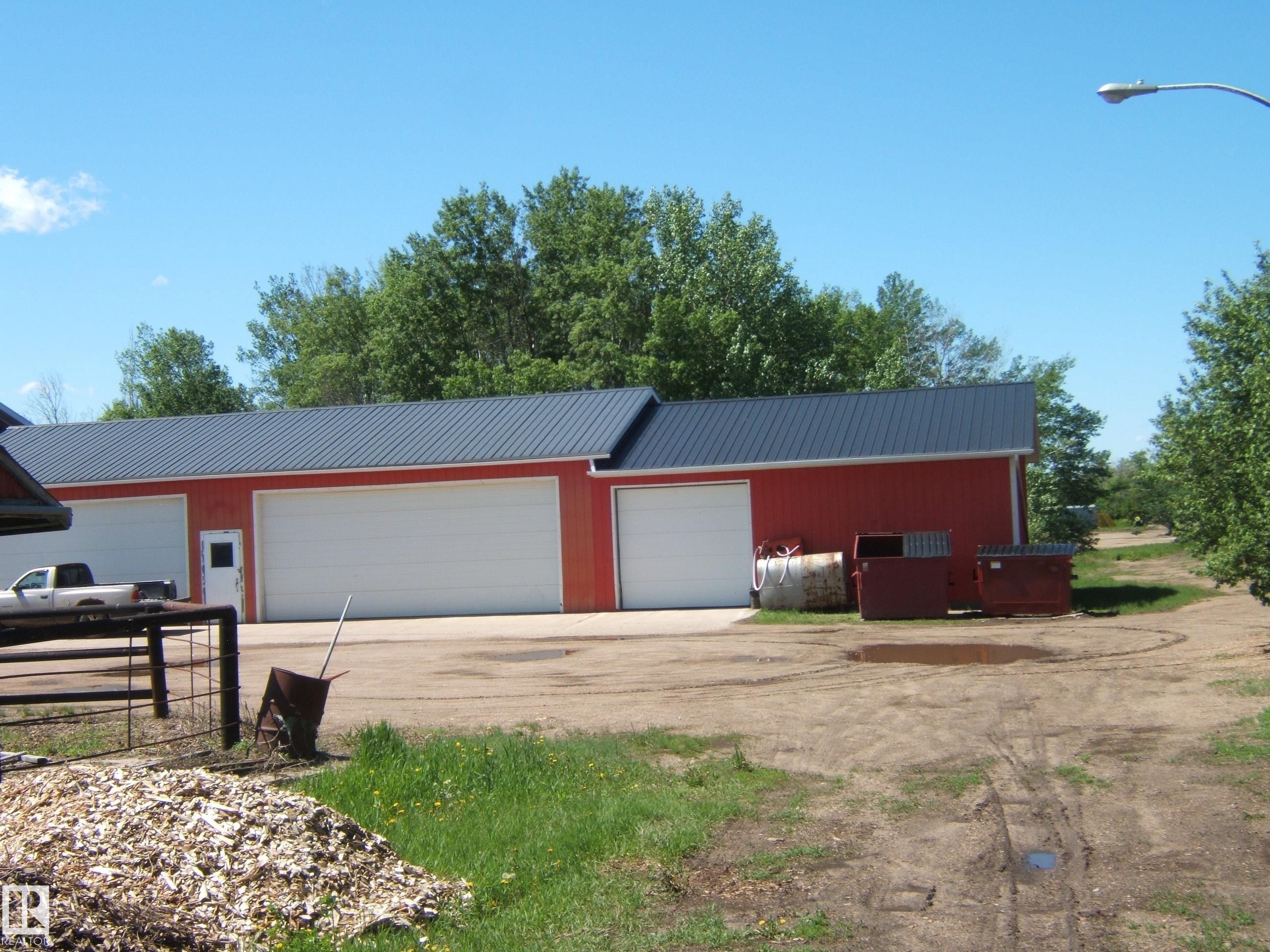 Red-sided outbuilding with a dark metal roof, featuring multiple white garage doors and a pedestrian door - 123064 Hwy 45, Rural Two Hills County, AB