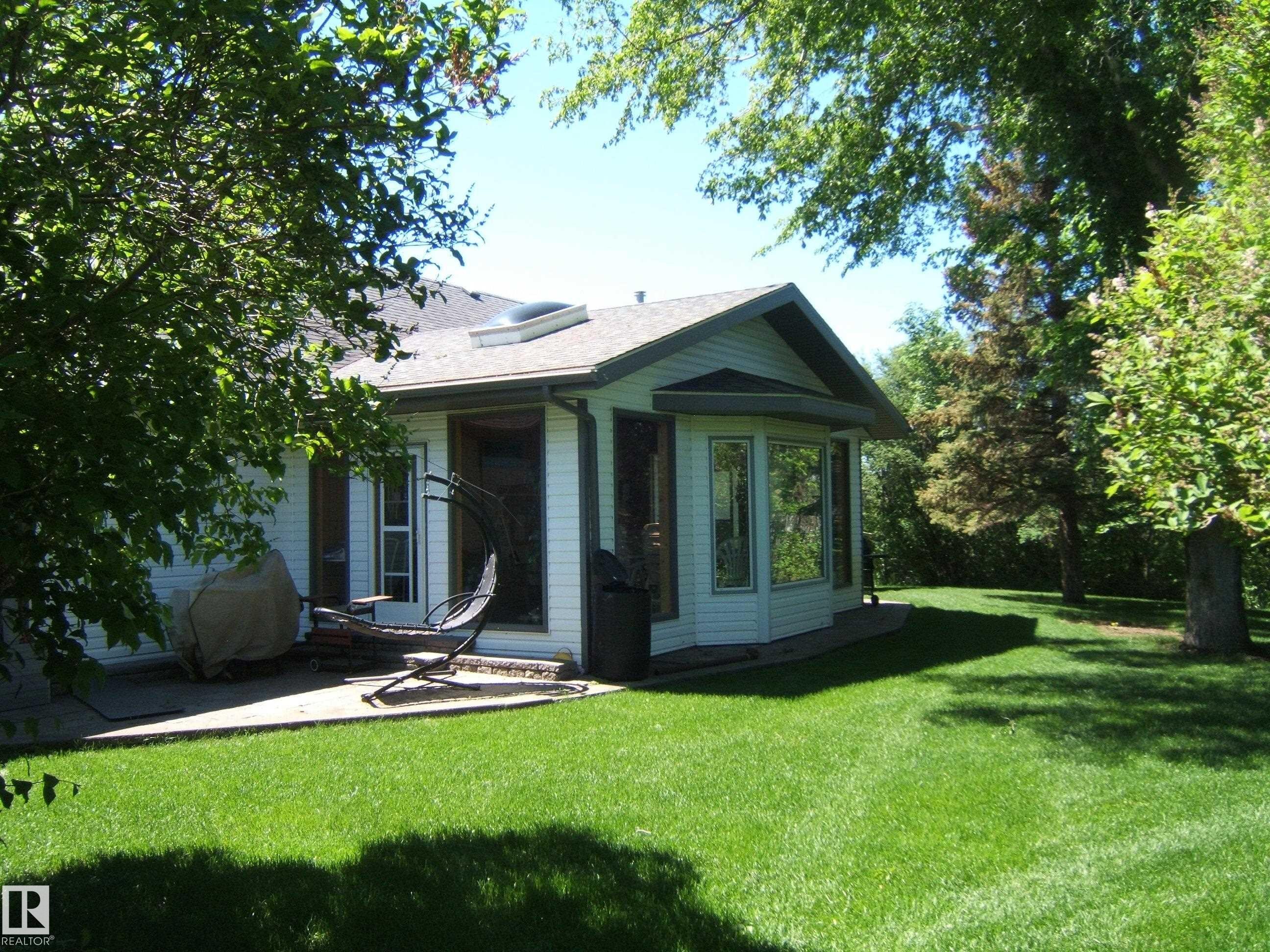 Spacious green lawn with mature trees and a concrete patio - 123064 Hwy 45, Rural Two Hills County, AB