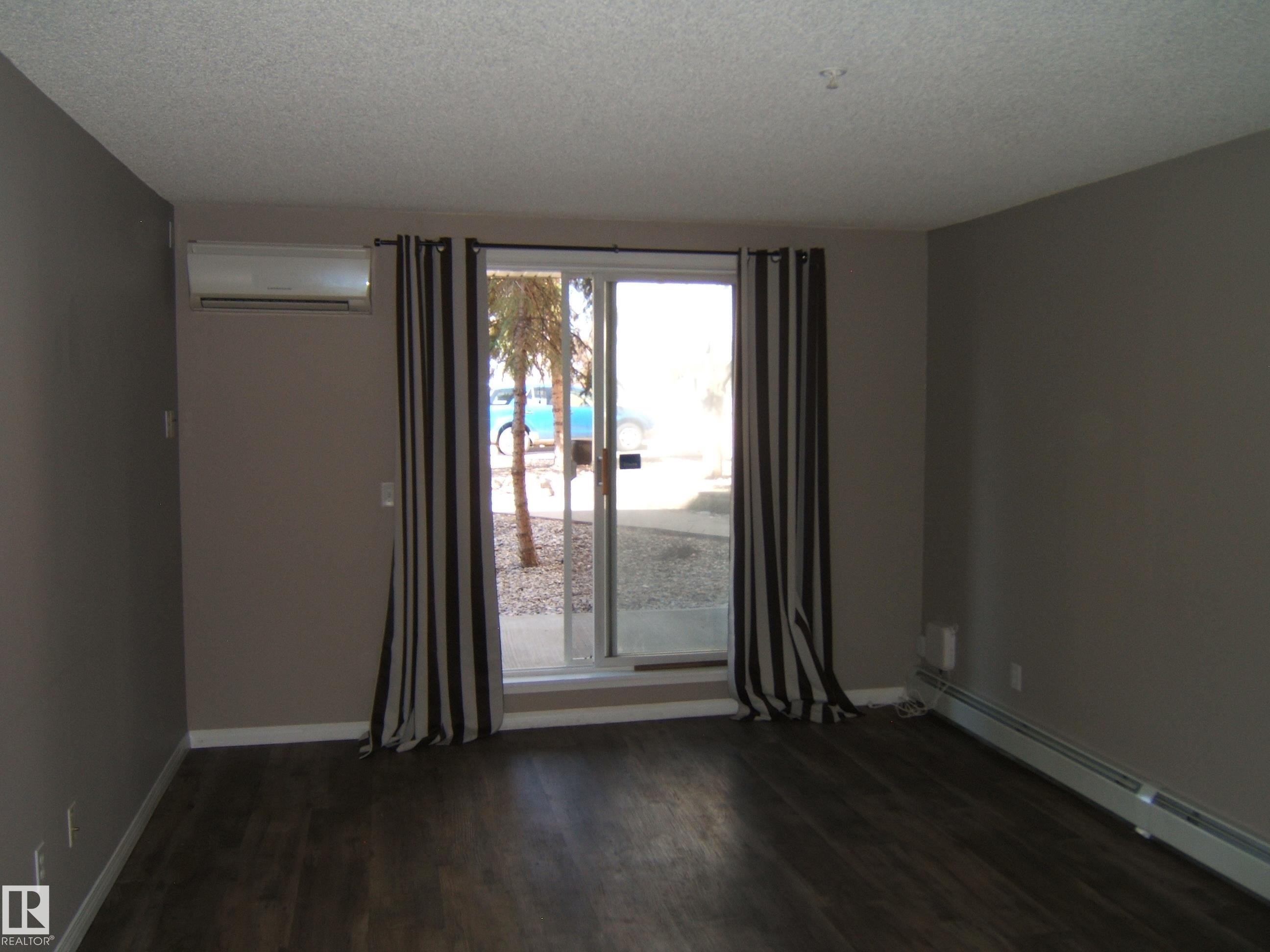 Interior living space featuring dark wood-finish flooring, neutral-toned walls, and white baseboards - 105 11214 80 Street, Edmonton, AB - Indoor Photo Showing Other Room