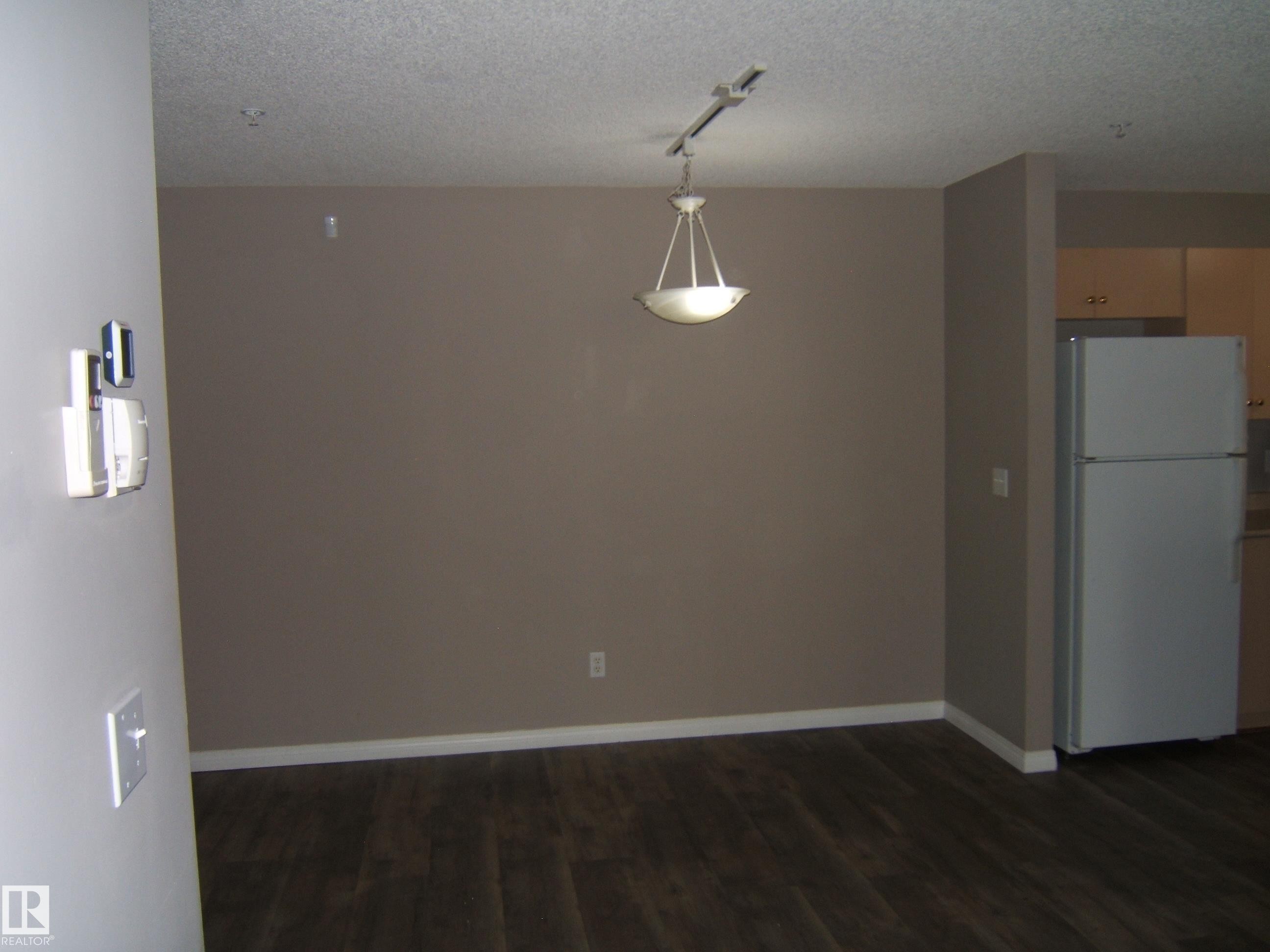 Spacious interior featuring dark wood-finish flooring, a contemporary pendant light fixture, and track lighting - 105 11214 80 Street, Edmonton, AB - Indoor