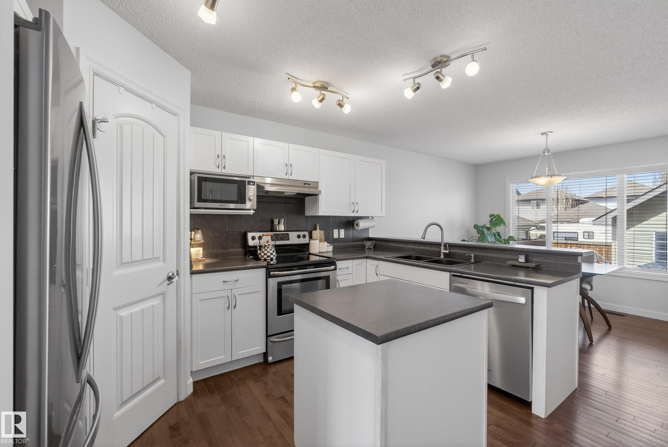 Contemporary kitchen featuring white cabinetry, dark countertops, a central island, and stainless steel appliances - 1148 35 Avenue, Edmonton, AB - Indoor Photo Showing Kitchen