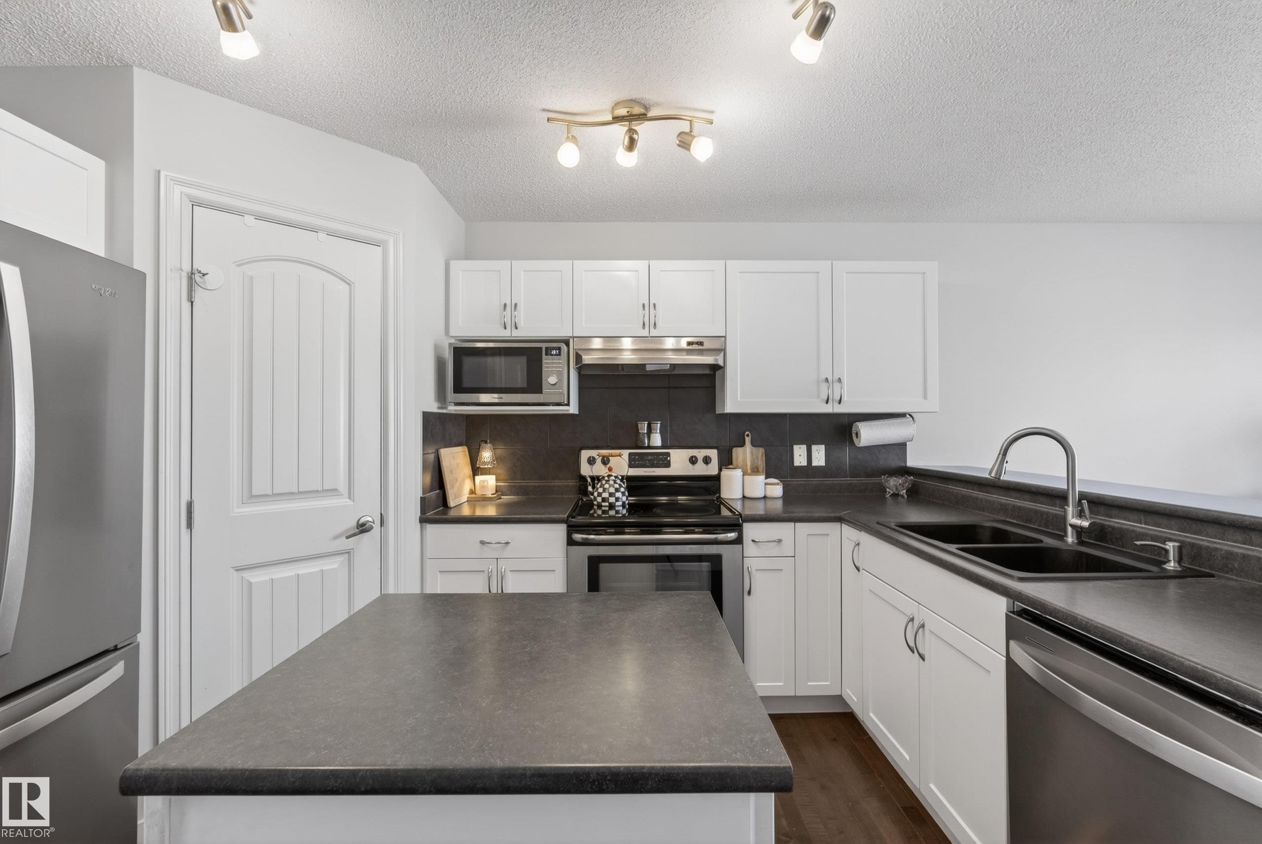Kitchen featuring white cabinetry, dark countertops, stainless steel appliances, and a central island - 1148 35 Avenue, Edmonton, AB - Indoor Photo Showing Kitchen With Double Sink