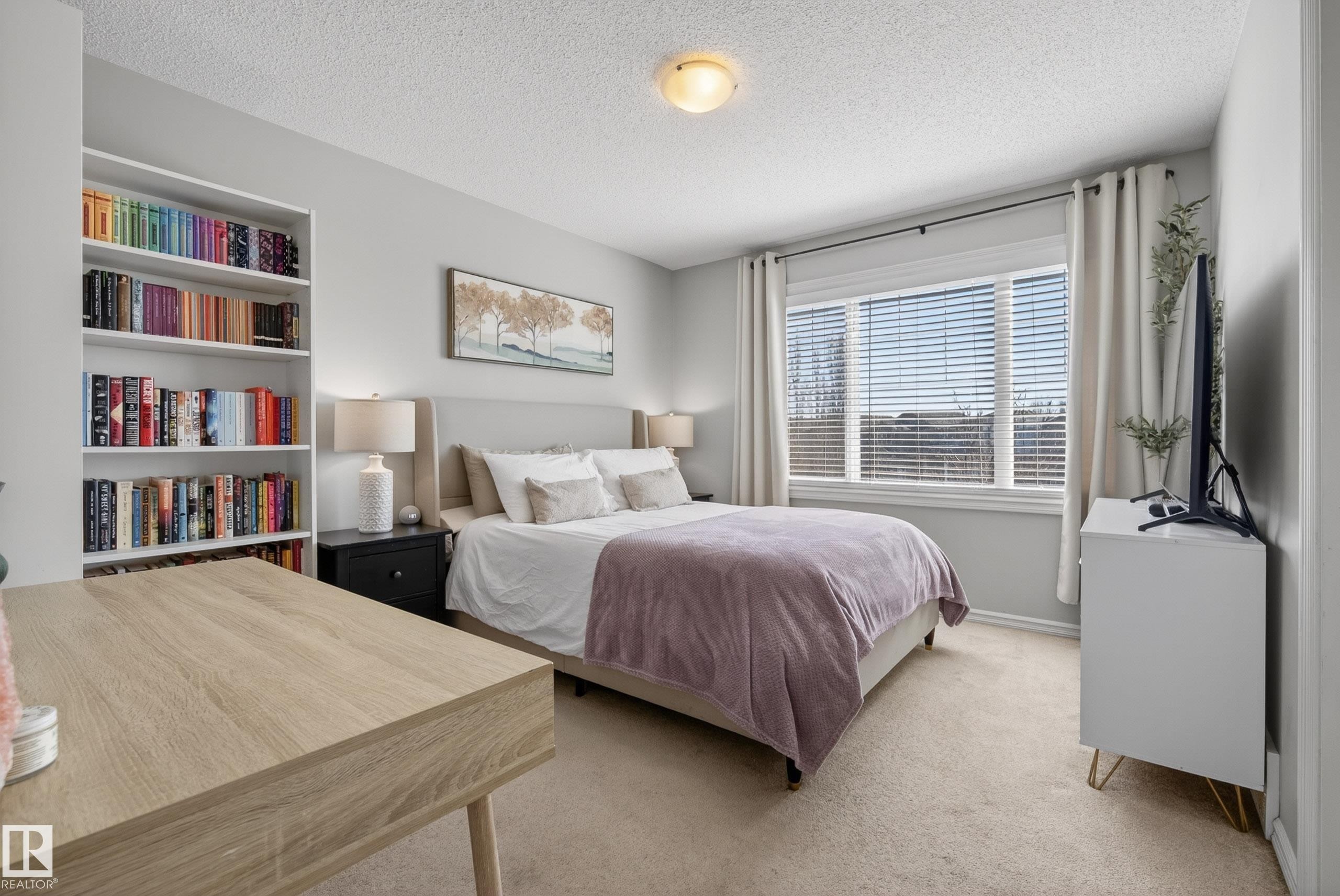 Carpeted room featuring a large window with blinds, a built-in shelving unit, and an overhead flush-mount light fixture - 1148 35 Avenue, Edmonton, AB - Indoor Photo Showing Bedroom