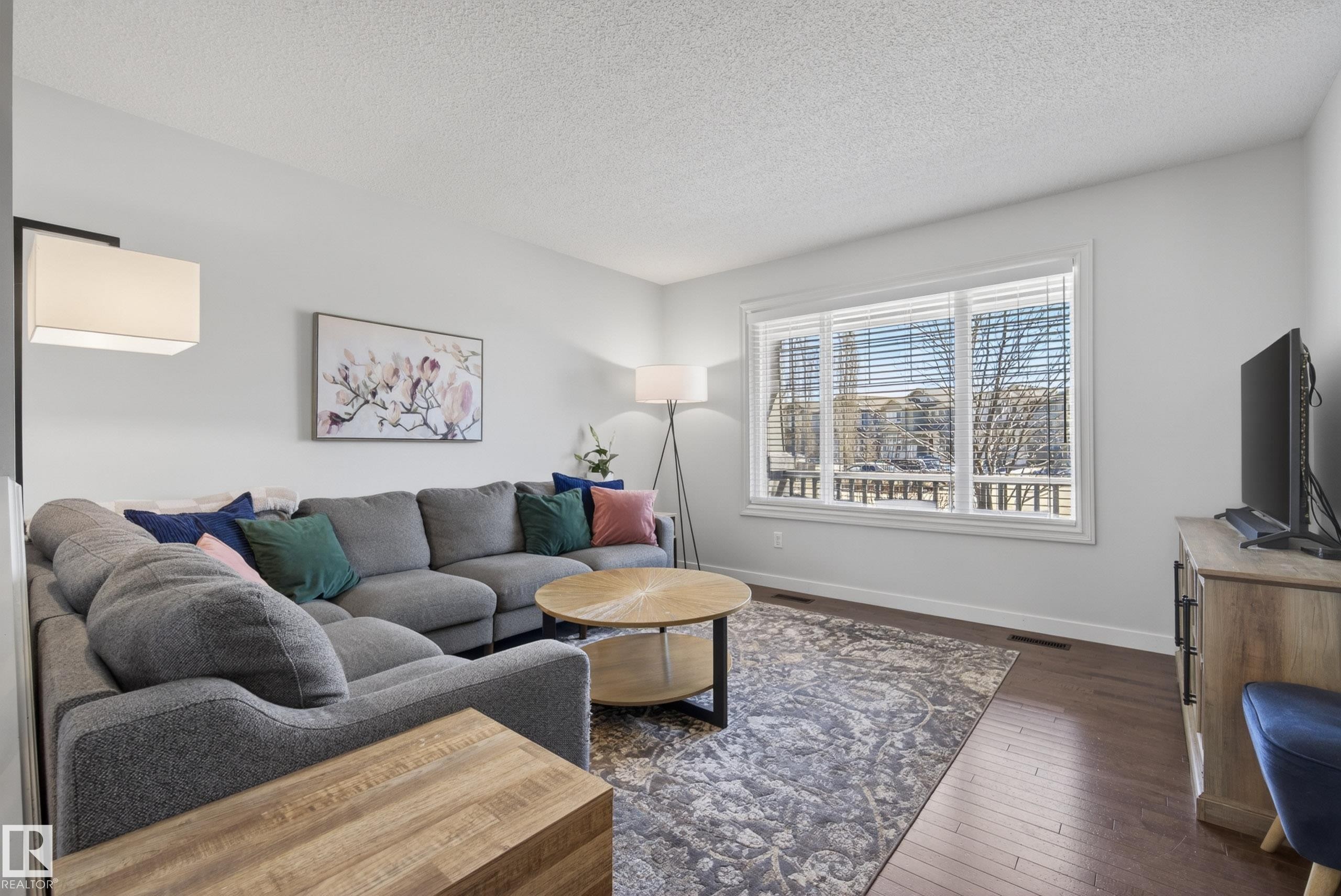 Living area featuring wood-finish flooring, a large picture window with blinds, and white painted walls - 1148 35 Avenue, Edmonton, AB - Indoor Photo Showing Living Room
