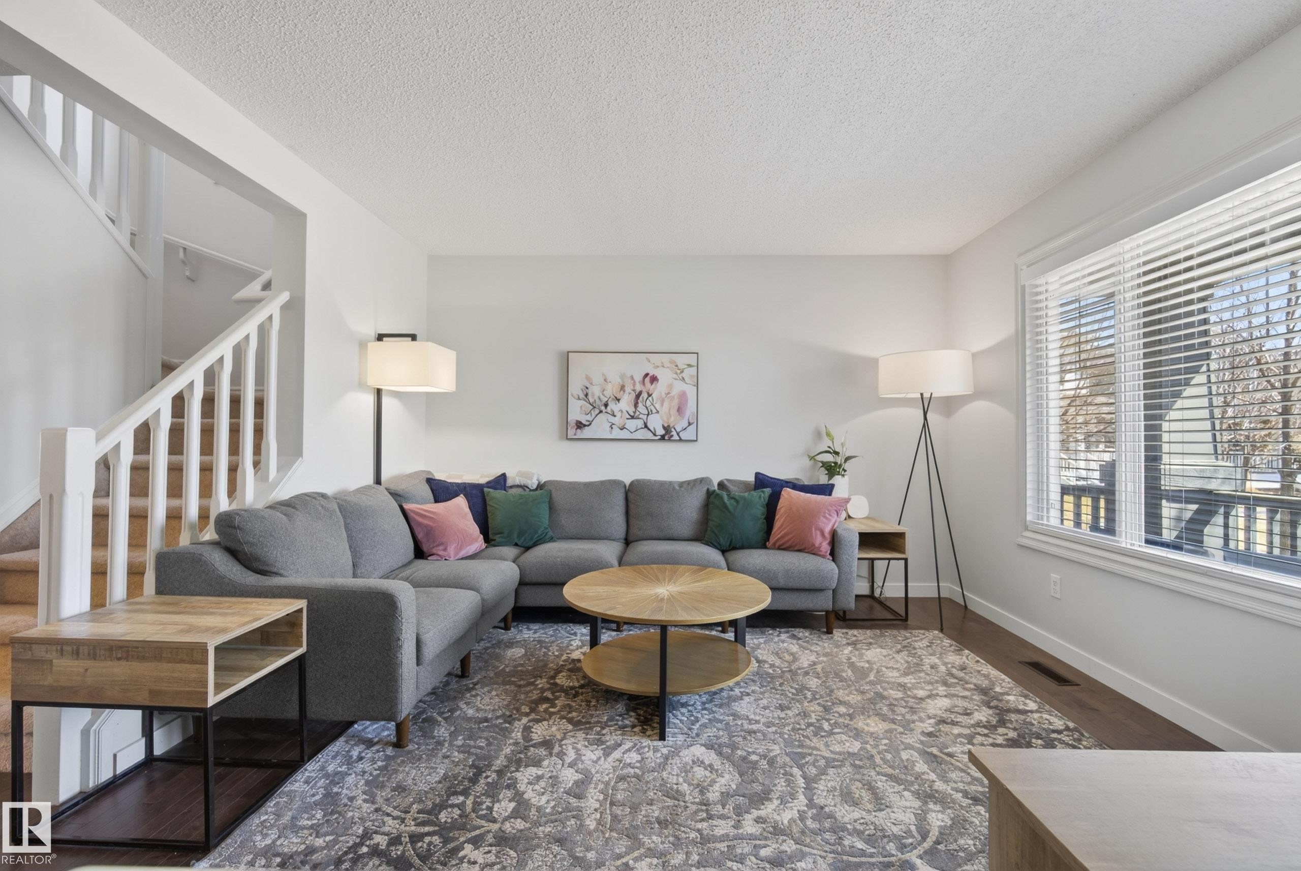 Spacious living area featuring large windows with blinds, dark wood-finish flooring, and white painted walls - 1148 35 Avenue, Edmonton, AB - Indoor Photo Showing Living Room