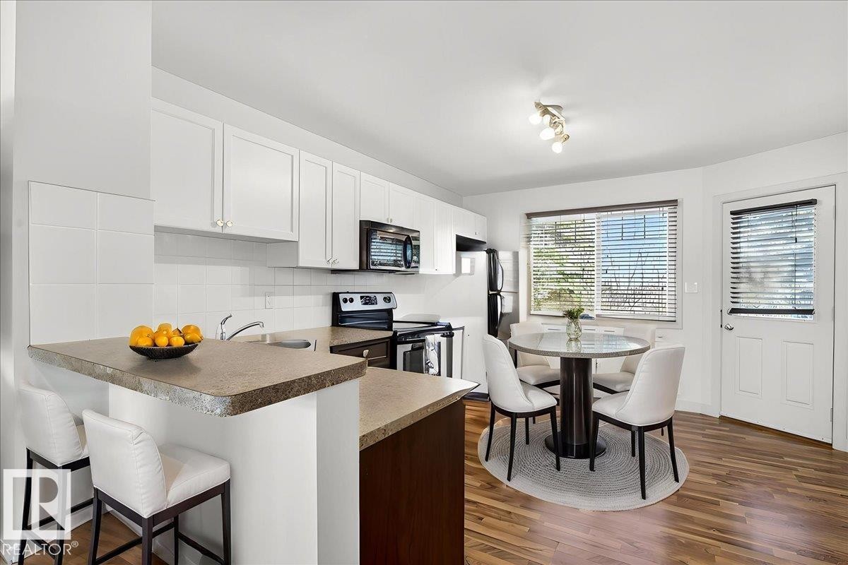 Bright kitchen featuring white cabinetry, a built-in microwave, and a black appliance suite - 18 6032 38 Avenue, Edmonton, AB - Indoor