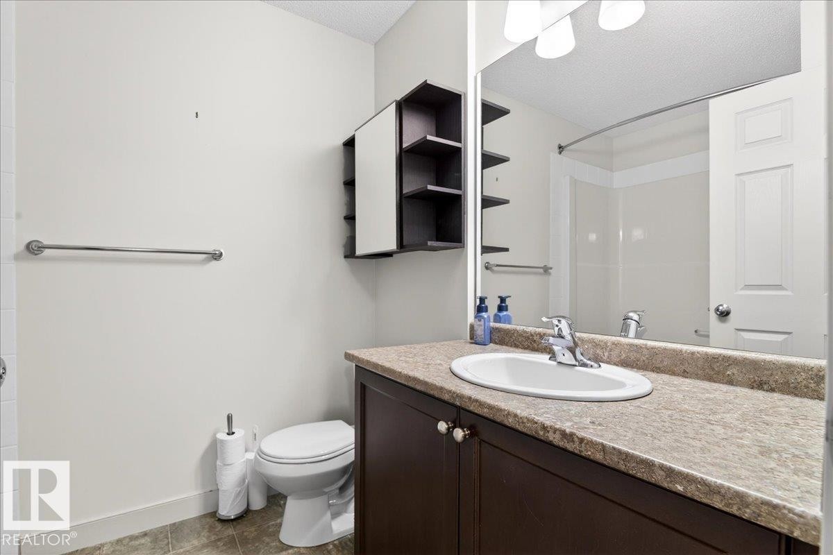 Bathroom featuring a dark wood-finish vanity with a light speckled countertop, an oval undermount sink, and a mirrored medicine cabinet with open shelving - 18 6032 38 Avenue, Edmonton, AB - Indoor Photo Showing Bathroom