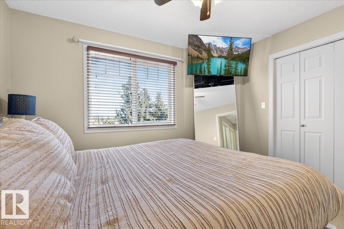 Inviting bedroom space featuring a window with horizontal blinds, neutral wall tones, a ceiling fan, and white bi-fold closet doors - 18 6032 38 Avenue, Edmonton, AB - Indoor Photo Showing Bedroom