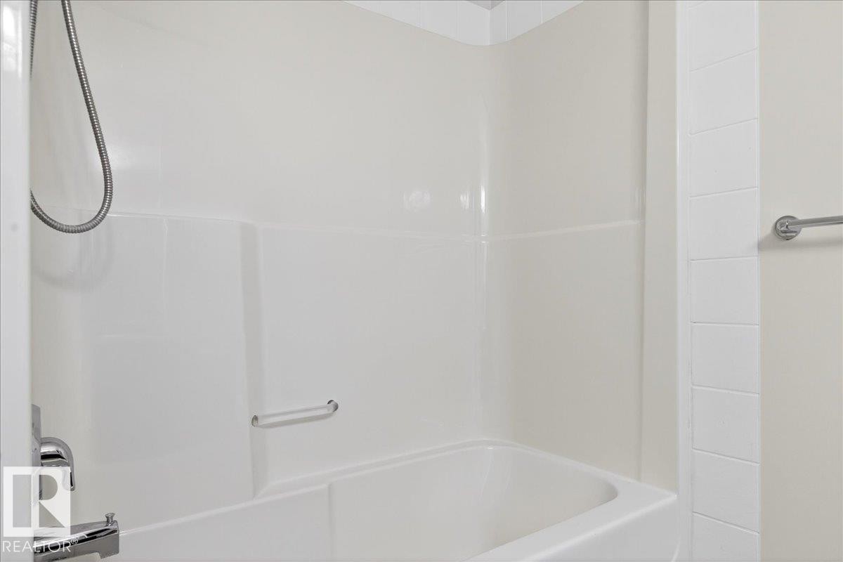White bathtub with integrated shower, chrome fixtures, and a wall-mounted towel bar - 18 6032 38 Avenue, Edmonton, AB - Indoor Photo Showing Bathroom