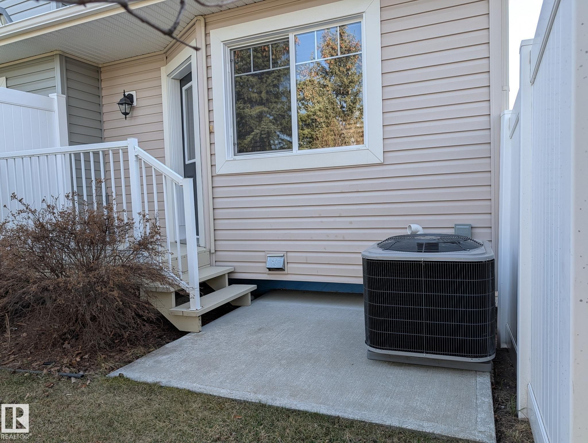 Rear exterior featuring beige horizontal siding, white trim, a concrete patio, and a central air conditioning unit - 18 6032 38 Avenue, Edmonton, AB - Outdoor With Exterior