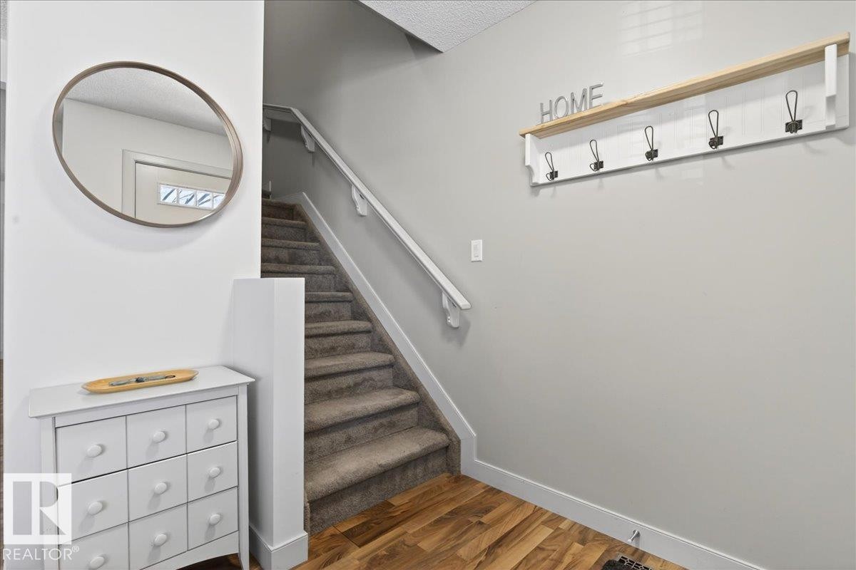 Inviting entryway featuring wood-finish flooring, a carpeted staircase with a white handrail, and a built-in coat rack with shelf - 18 6032 38 Avenue, Edmonton, AB - Indoor Photo Showing Other Room