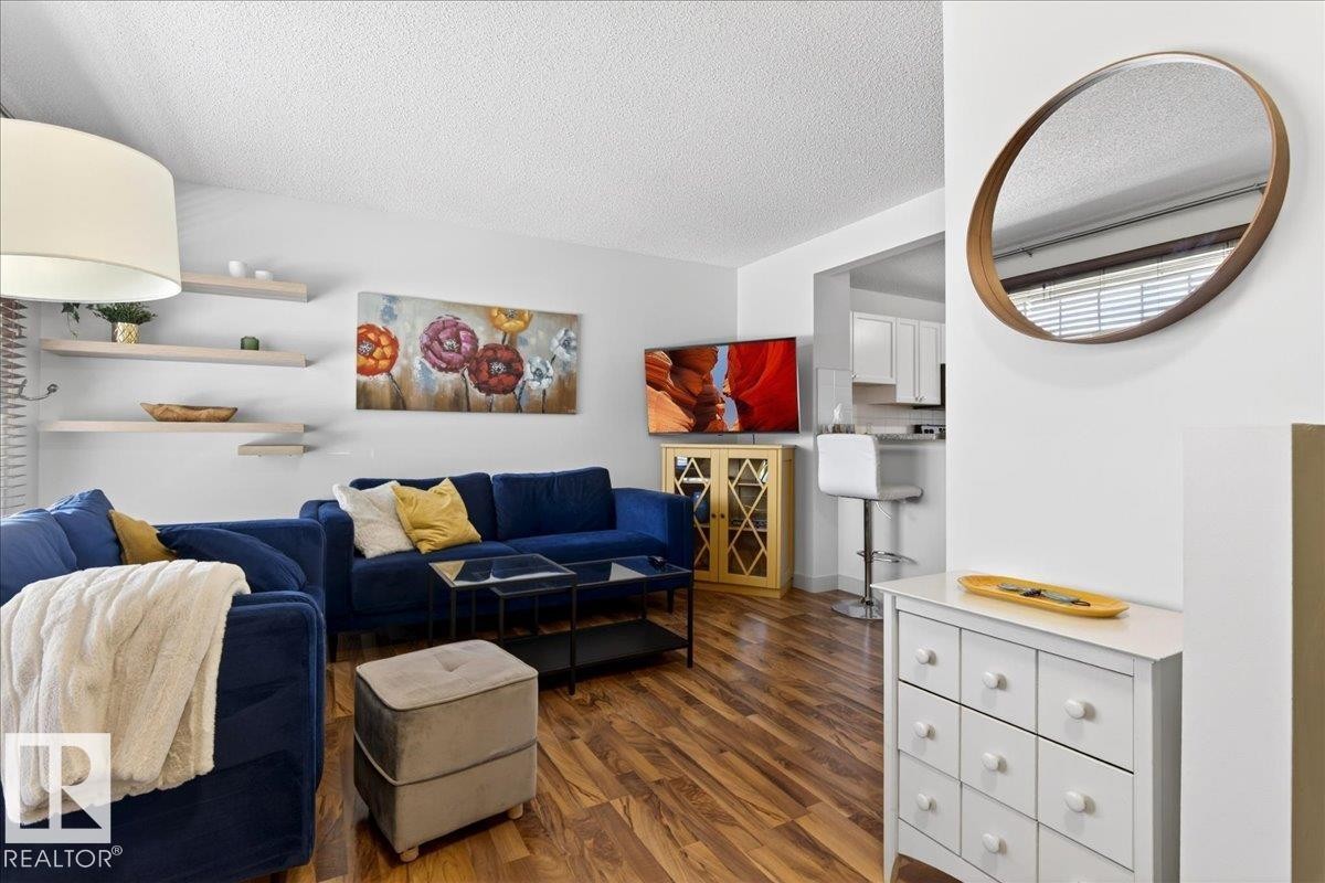 Open-concept living space featuring wood-finish flooring, white walls, and a recessed kitchen pass-through - 18 6032 38 Avenue, Edmonton, AB - Indoor Photo Showing Living Room
