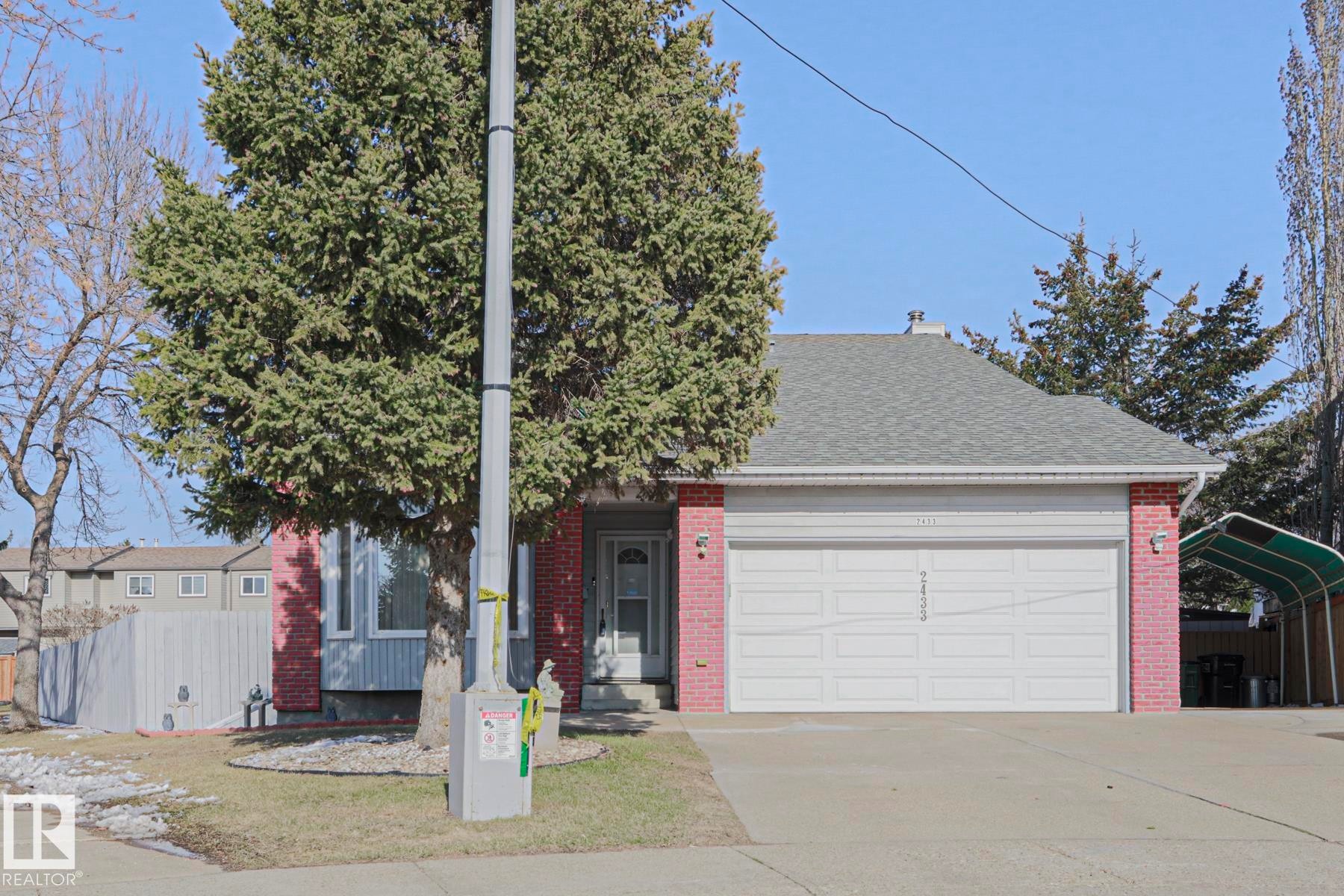 Brick facade home featuring an attached two-car garage, a covered front entry, and a mature evergreen tree - 2433 89 Street, Edmonton, AB - Outdoor