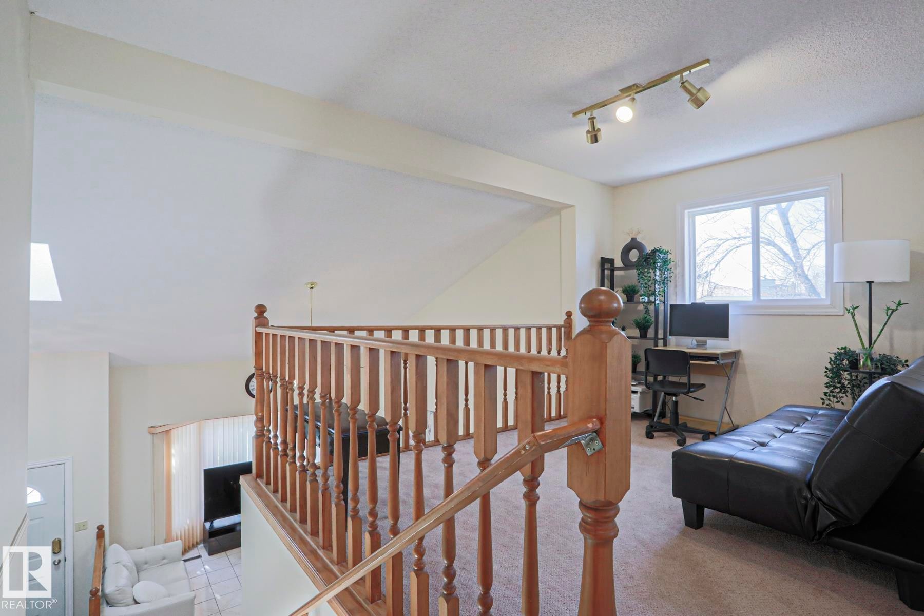 Upper level featuring wood baluster railing, carpet flooring, a white-framed window, and track lighting - 2433 89 Street, Edmonton, AB - Indoor