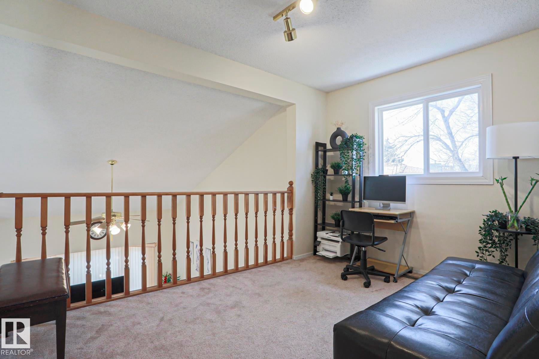 Carpeted loft area featuring a wooden railing, a double-pane window, and track lighting - 2433 89 Street, Edmonton, AB - Indoor