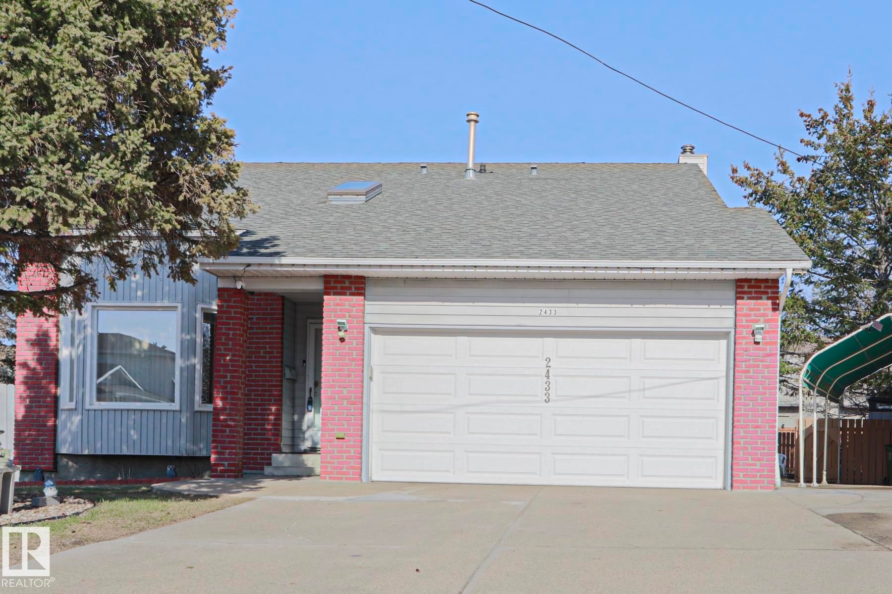 The exterior features a two-car garage with a panel door, a concrete driveway, and a shingled roof with a skylight - 2433 89 Street, Edmonton, AB - Outdoor