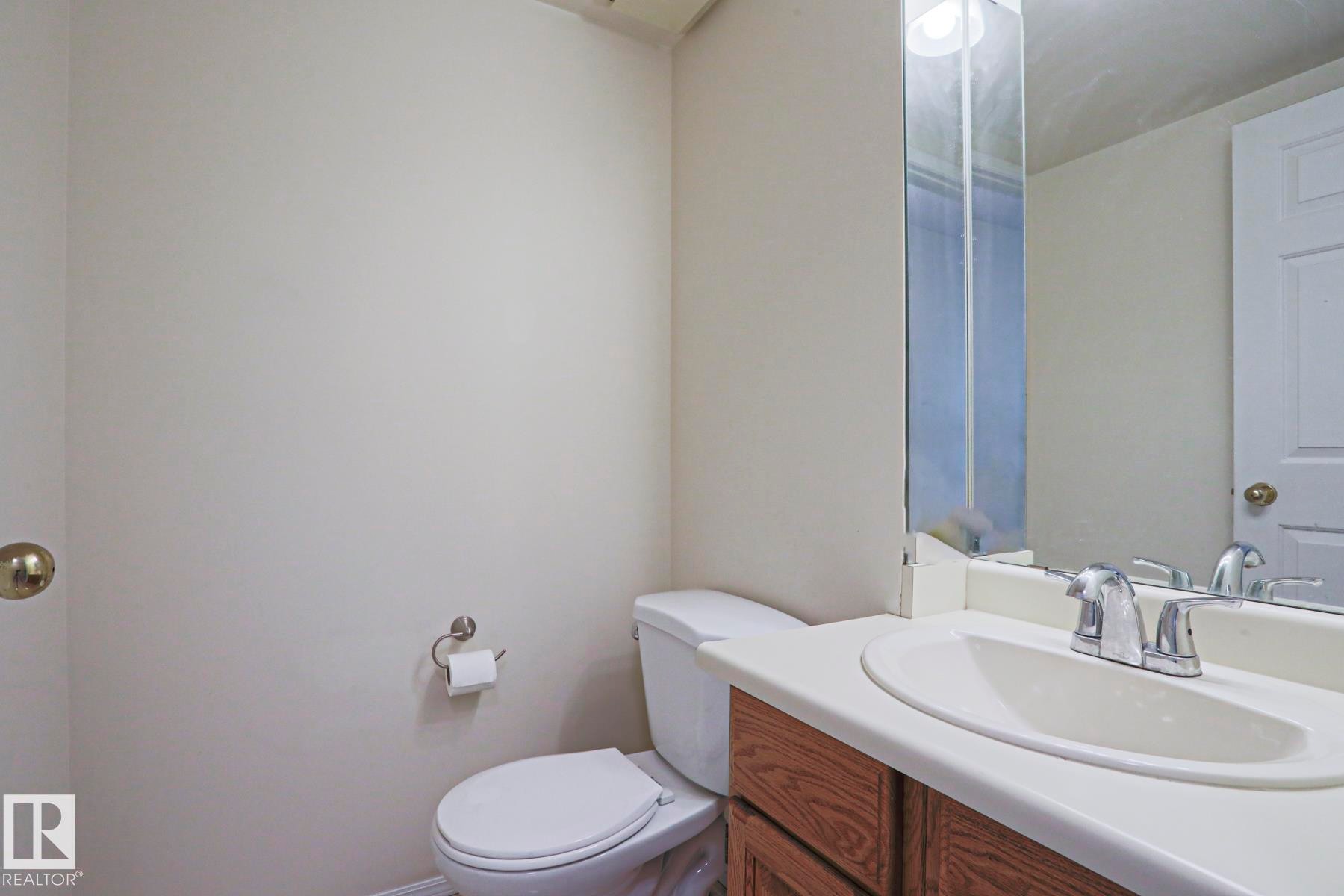 Powder room featuring a white single-sink vanity with wood-finish cabinetry, a chrome faucet, and a large wall-mounted mirror - 2433 89 Street, Edmonton, AB - Indoor Photo Showing Bathroom