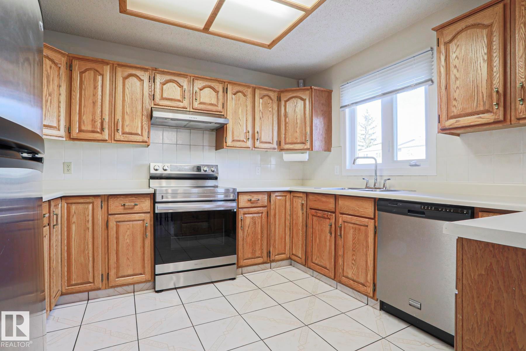 Kitchen featuring wood cabinetry, white countertops, tile flooring, a stainless steel range, and a stainless steel dishwasher - 2433 89 Street, Edmonton, AB - Indoor Photo Showing Kitchen