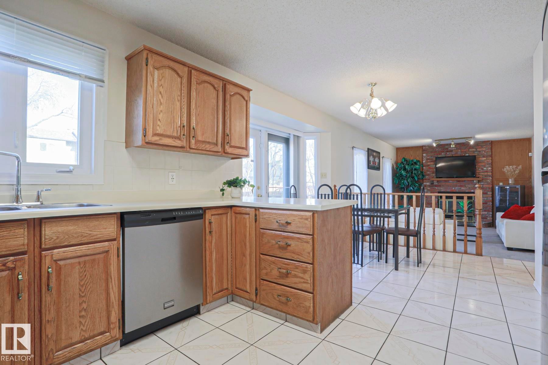 Kitchen featuring wood cabinetry, a stainless steel dishwasher, and white tile flooring - 2433 89 Street, Edmonton, AB - Indoor Photo Showing Kitchen