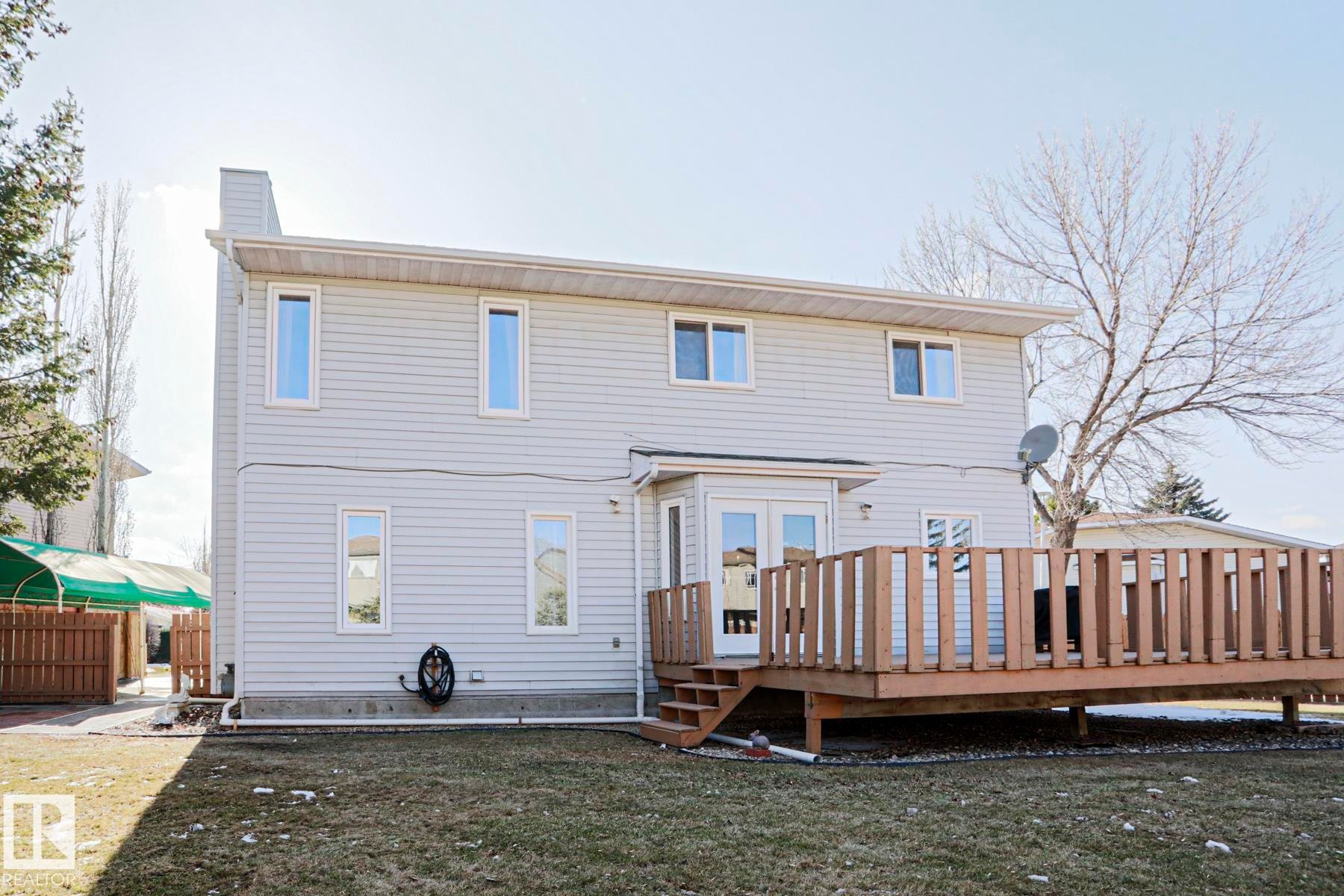 Rear exterior featuring light-colored siding, a multi-level wood deck, and a grass lawn - 2433 89 Street, Edmonton, AB - Outdoor With Deck Patio Veranda With Exterior