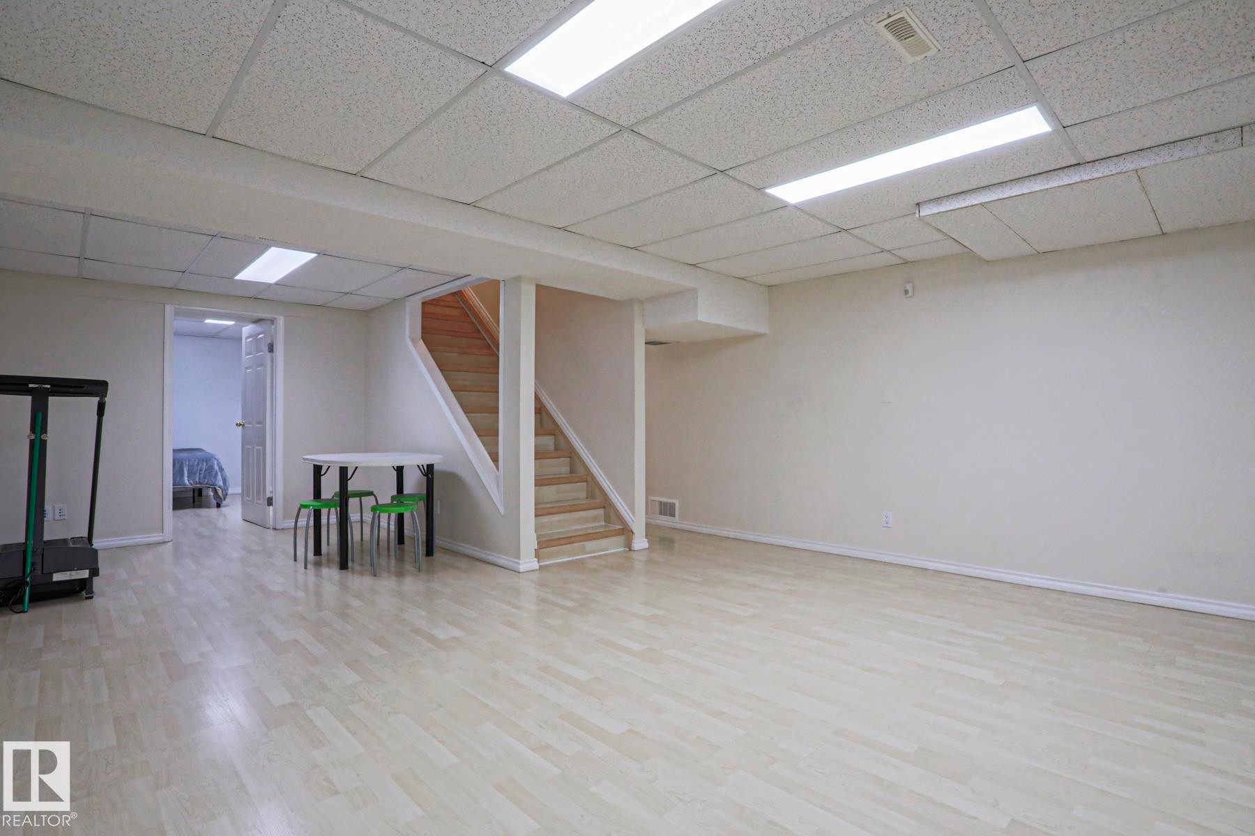 Spacious lower-level room featuring light wood-finish flooring and a drop ceiling with integrated fluorescent lighting - 2433 89 Street, Edmonton, AB - Indoor Photo Showing Basement