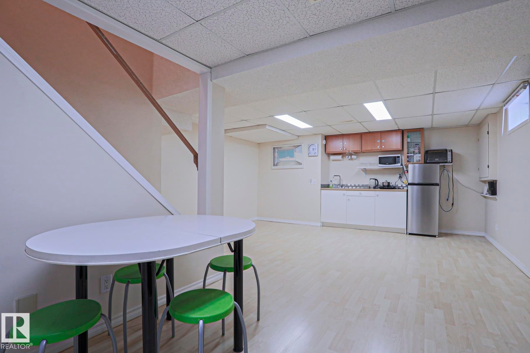 Spacious lower-level area featuring wood-finish flooring, a built-in kitchenette with wood cabinetry, a stainless steel refrigerator, and recessed lighting - 2433 89 Street, Edmonton, AB - Indoor Photo Showing Basement