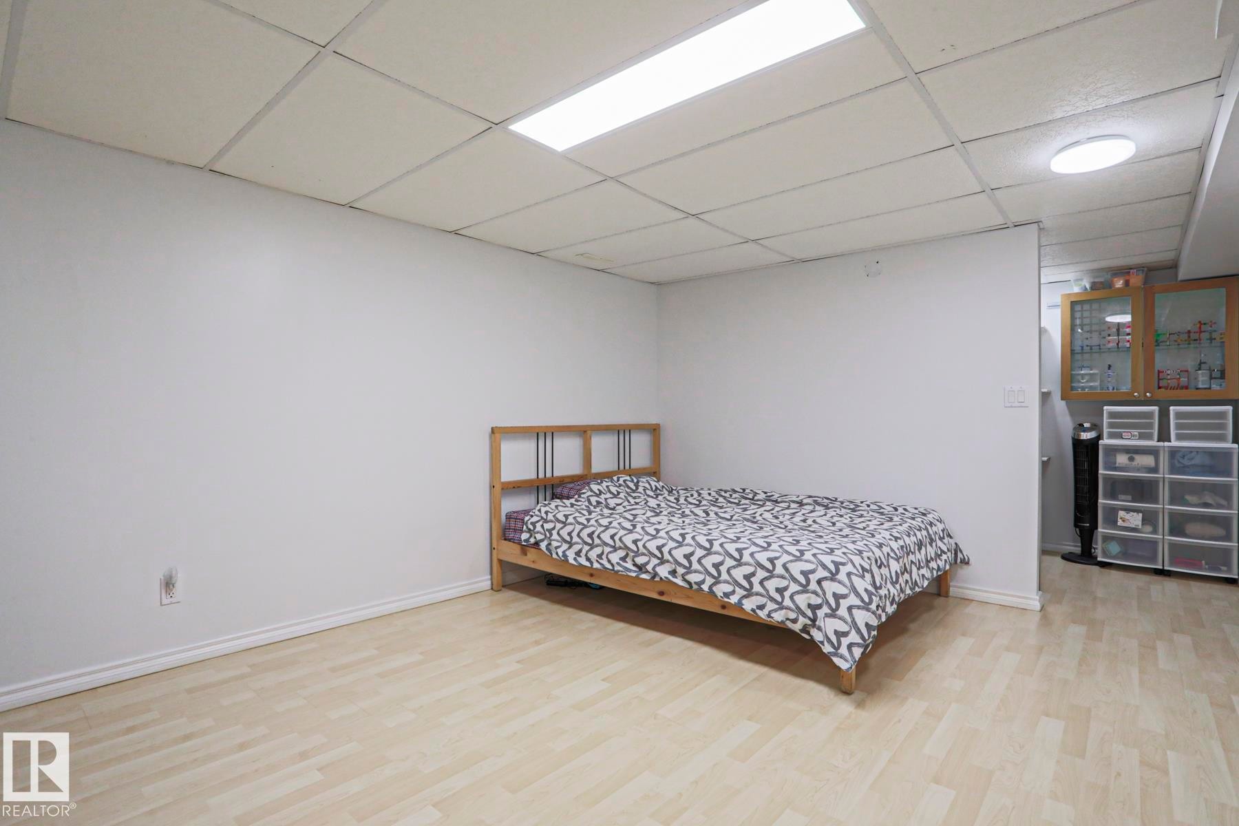 Spacious room featuring light wood-finish flooring, white baseboards, and a dropped ceiling with integrated lighting - 2433 89 Street, Edmonton, AB - Indoor Photo Showing Bedroom