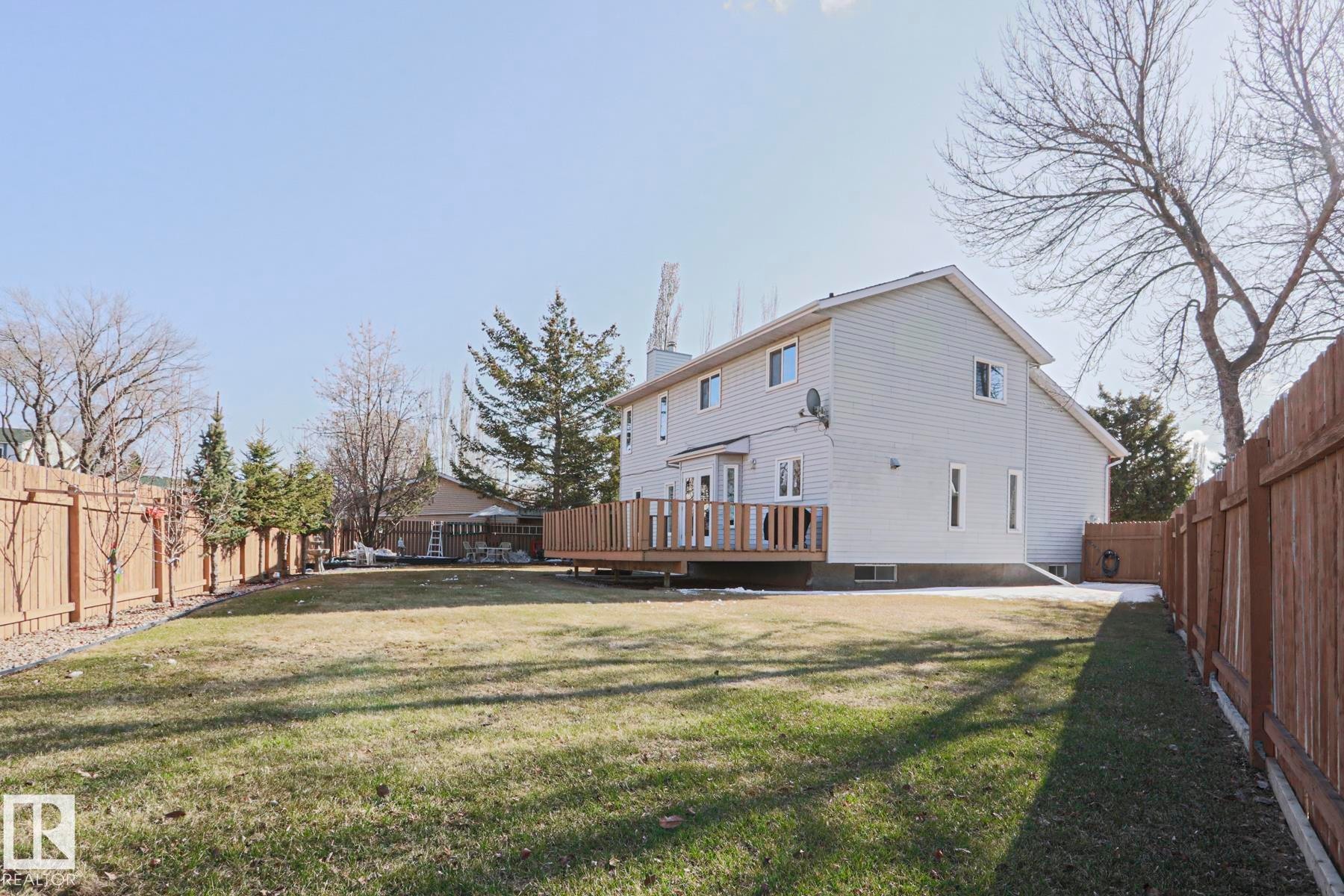 Expansive fenced backyard featuring a generously sized wood-finish deck, mature perimeter trees, and a manicured lawn - 2433 89 Street, Edmonton, AB - Outdoor With Deck Patio Veranda