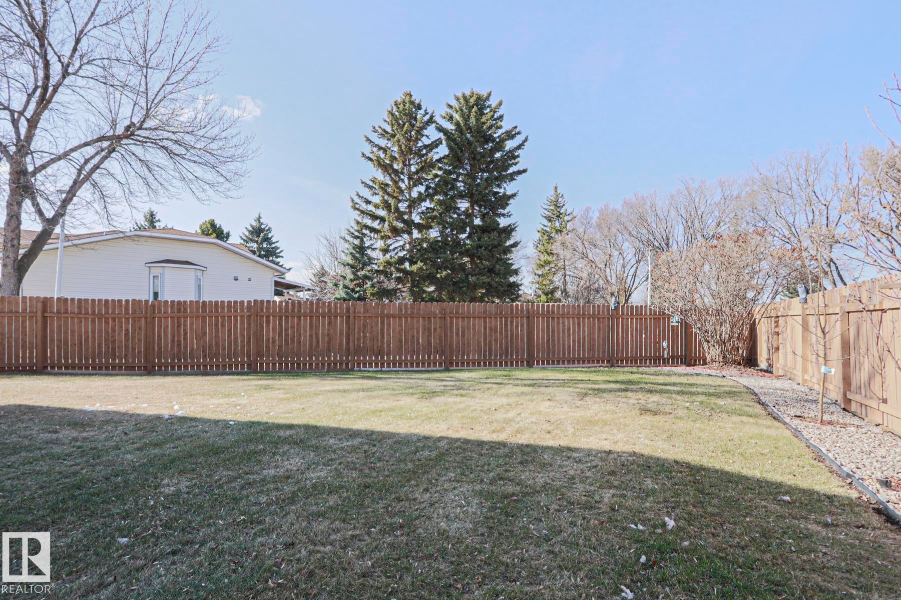 Spacious backyard featuring a manicured lawn, full-height privacy fencing, and a gravel border with young trees - 2433 89 Street, Edmonton, AB - Outdoor