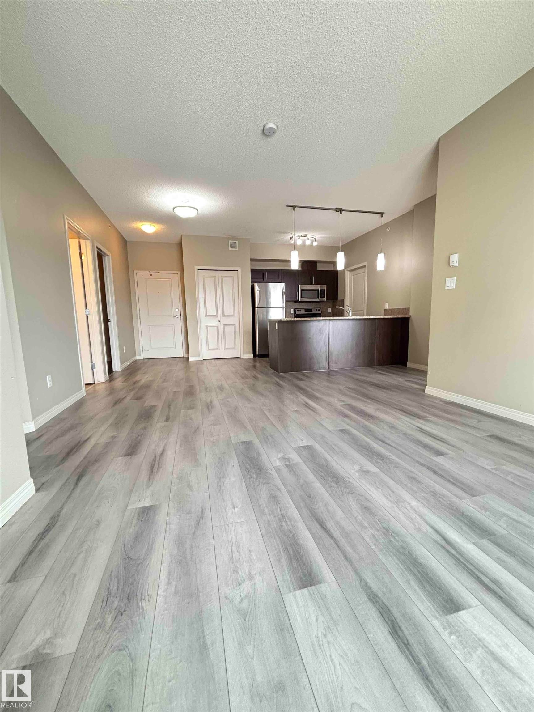 Expansive open-concept living area featuring wood-finish flooring, recessed lighting, and light-toned walls - 408 111 Ambelside Drive Sw, Edmonton, AB - Indoor