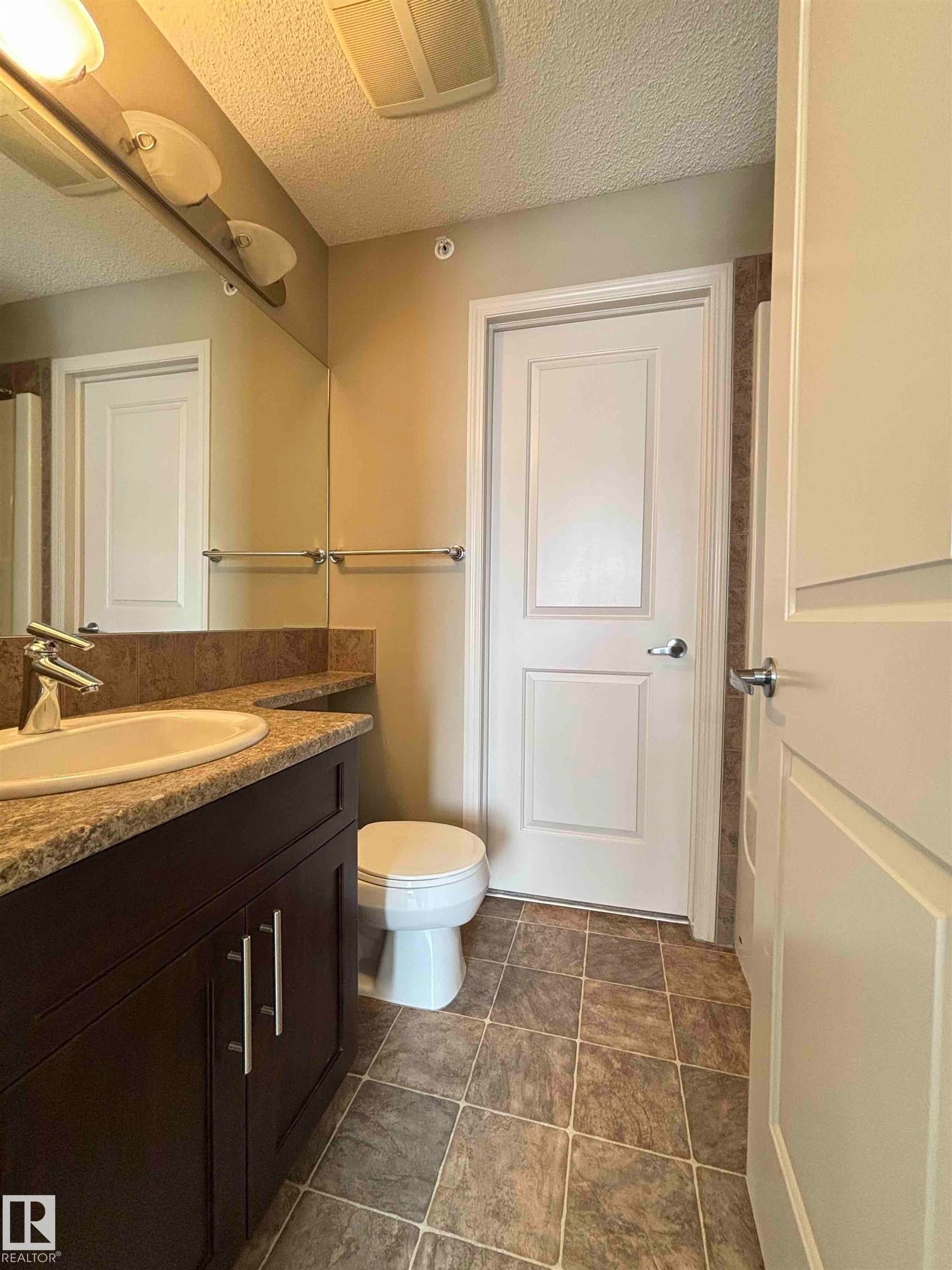 Bathroom featuring a dark wood-finish vanity with a drop-in sink, a speckled countertop, and tiled flooring - 408 111 Ambelside Drive Sw, Edmonton, AB - Indoor Photo Showing Bathroom