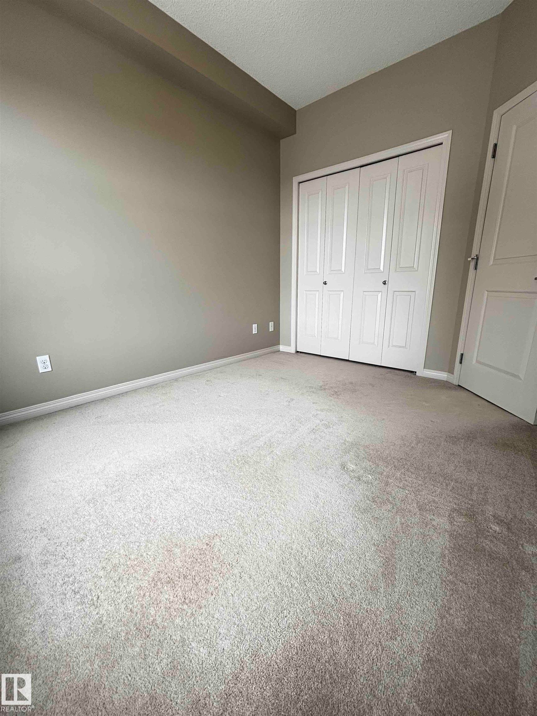 Carpeted room featuring a neutral wall color, white baseboards, and a bi-fold closet with white doors - 408 111 Ambelside Drive Sw, Edmonton, AB - Indoor Photo Showing Other Room
