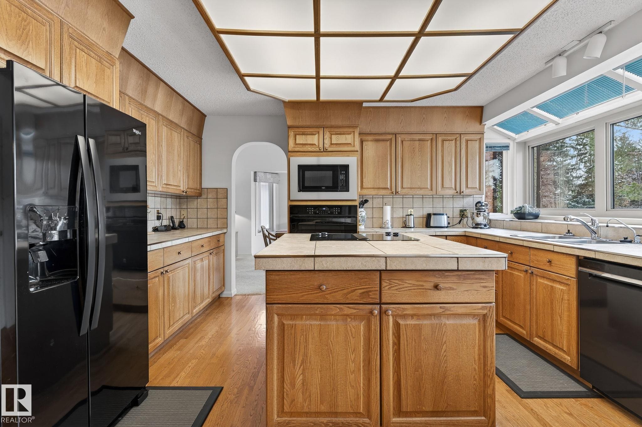 Well-appointed kitchen featuring wood-finish cabinetry, tile countertops, and a central island - 848 Wheeler Road W, Edmonton, AB - Indoor Photo Showing Kitchen With Double Sink