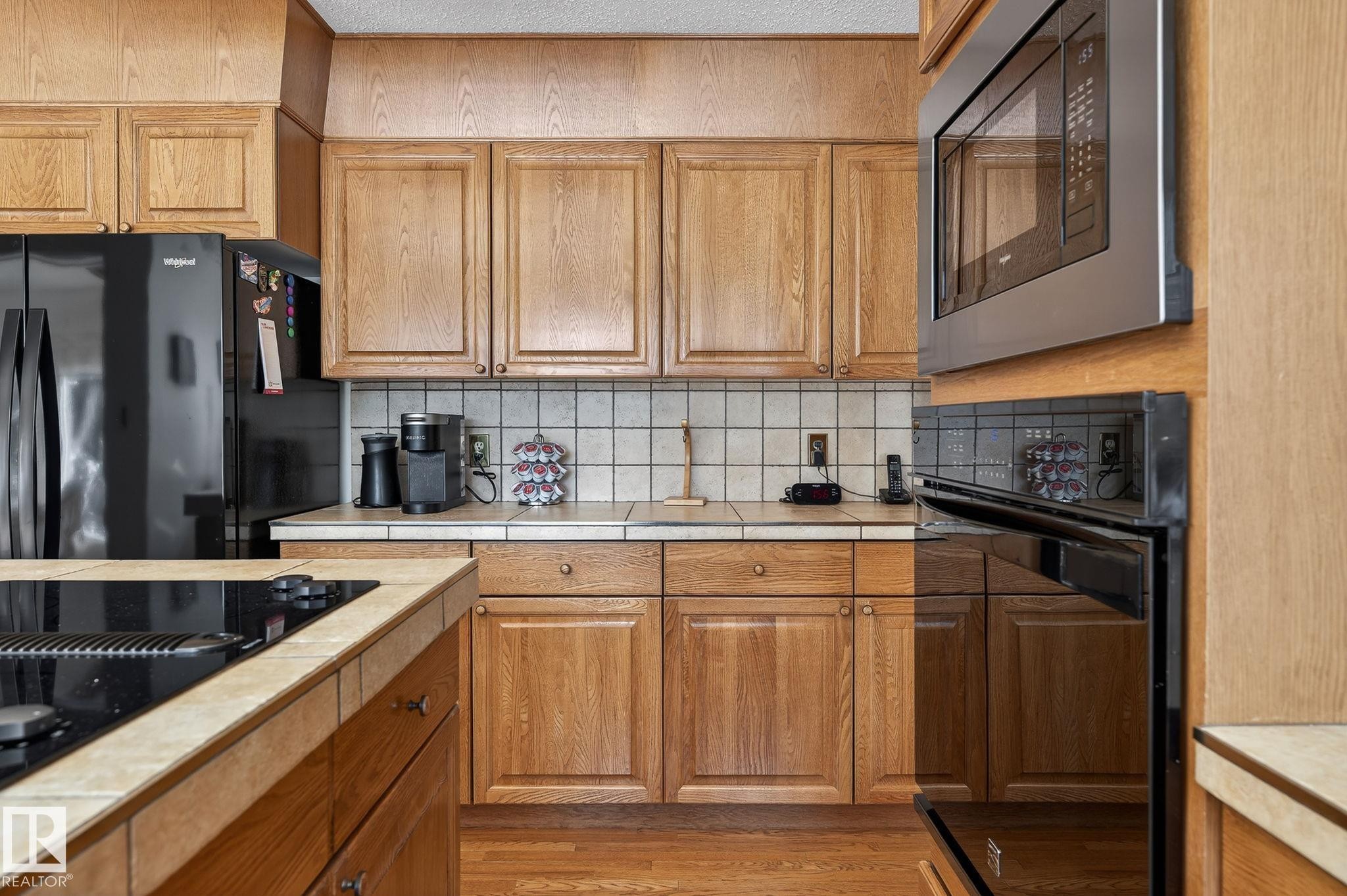 Kitchen featuring wood-finish cabinetry, tile countertops, and a white square tile backsplash - 848 Wheeler Road W, Edmonton, AB - Indoor Photo Showing Kitchen
