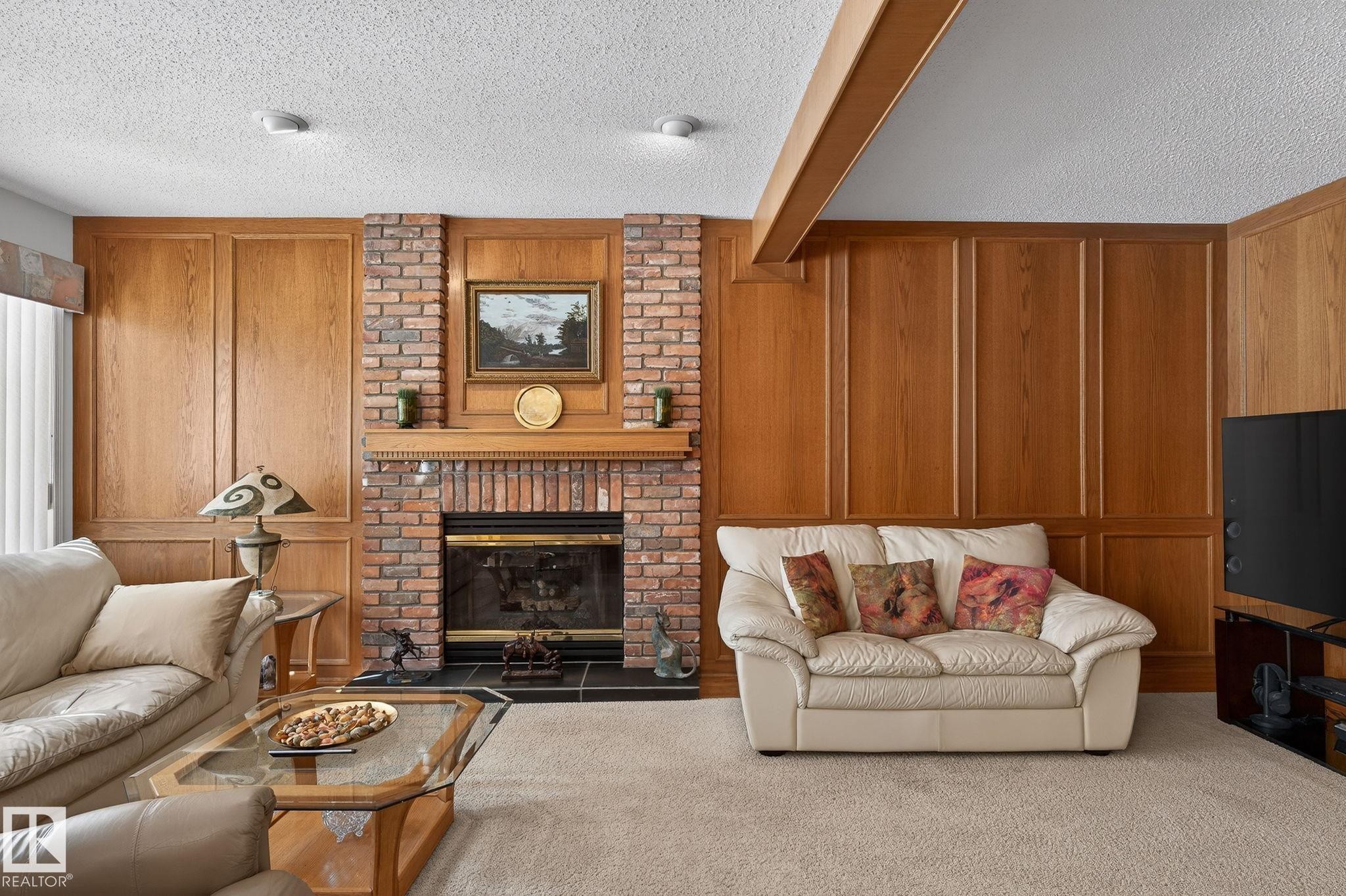 Brick fireplace with a wood-finish mantel and black hearth, framed by extensive wood-paneled walls - 848 Wheeler Road W, Edmonton, AB - Indoor Photo Showing Living Room With Fireplace