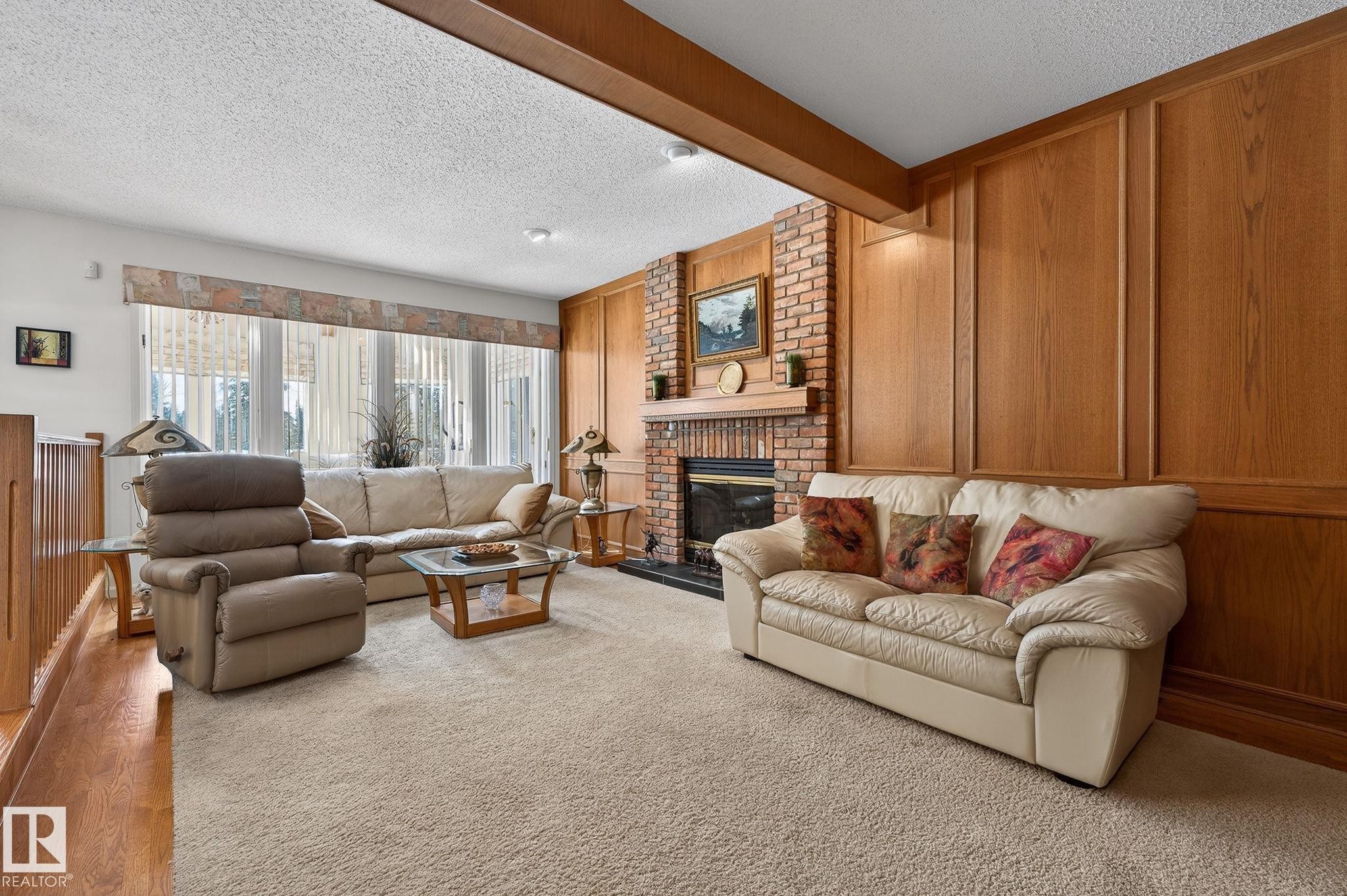 Spacious living area featuring a brick-faced fireplace with a mantel, extensive wood paneling, and a large window wall - 848 Wheeler Road W, Edmonton, AB - Indoor Photo Showing Living Room With Fireplace