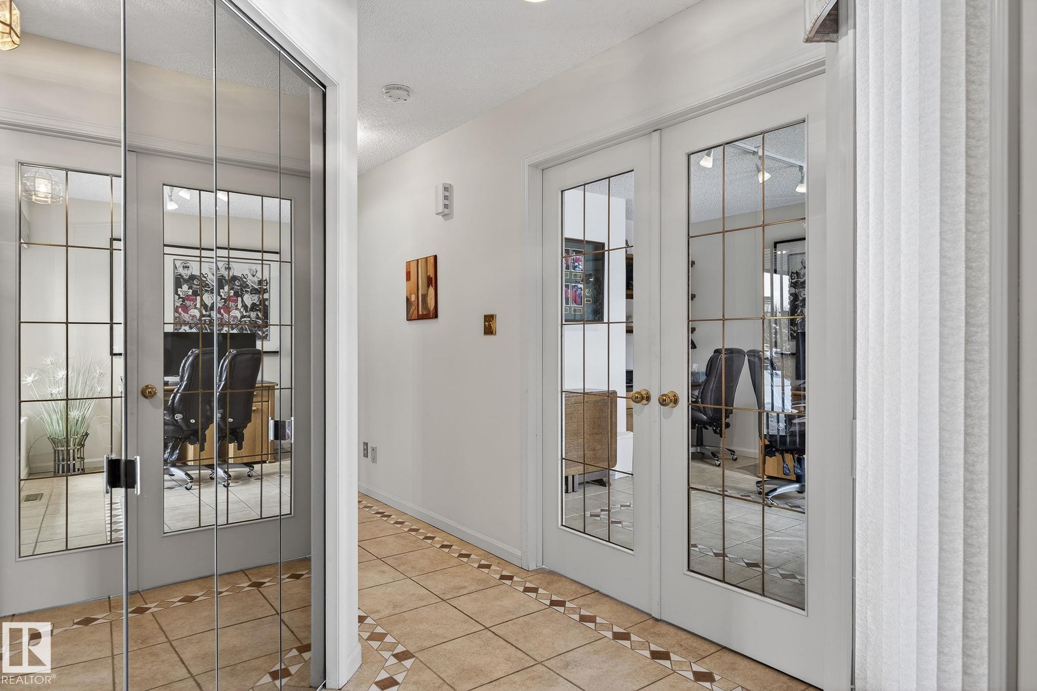 Hallway featuring tile flooring with decorative inlay, white walls, and two sets of double French doors with grid-patterned glass panels - 848 Wheeler Road W, Edmonton, AB - Indoor Photo Showing Other Room