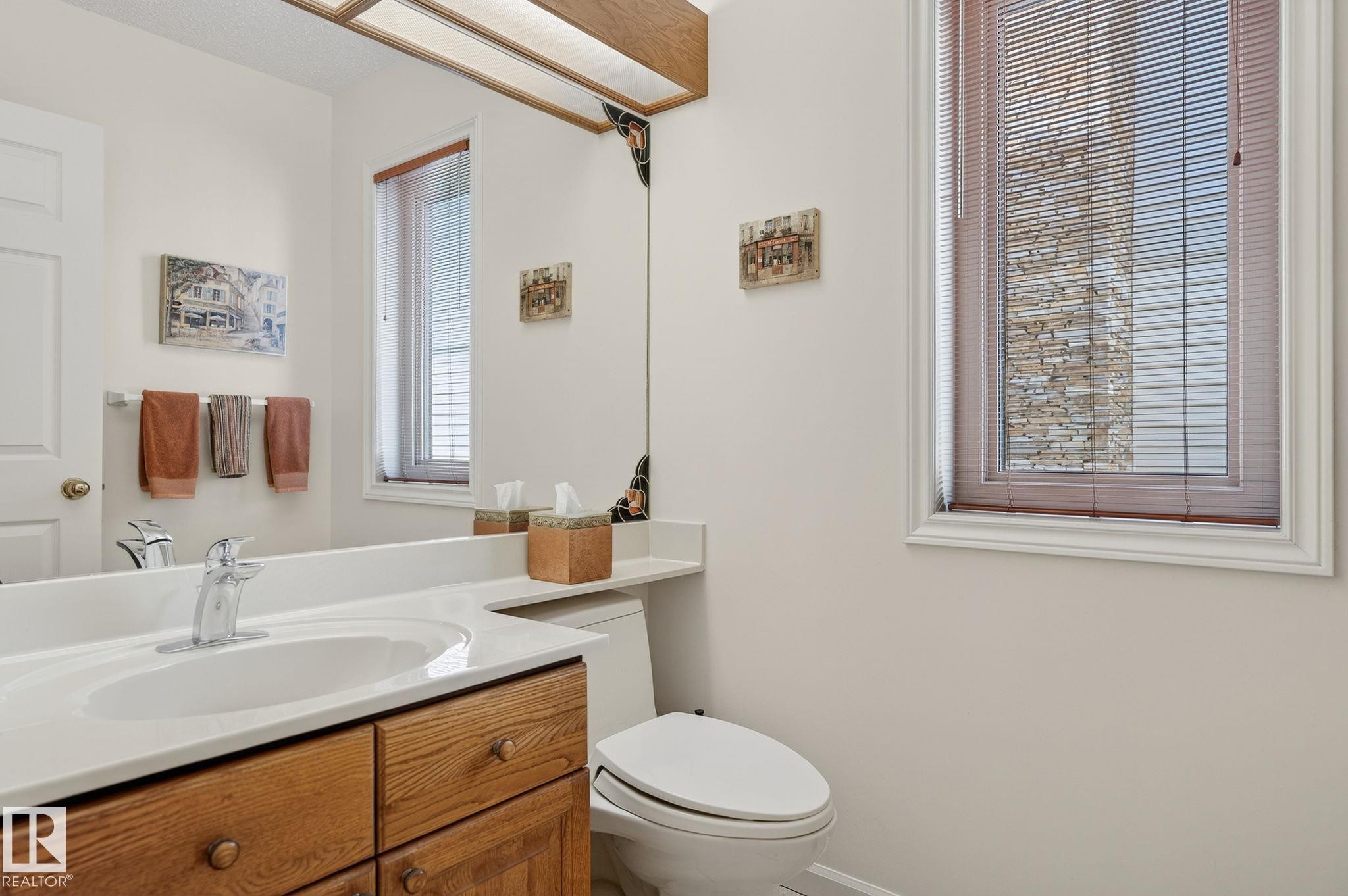 Bathroom featuring a wood-finish vanity with an integrated sink, polished chrome faucet, and a large wall-mounted mirror - 848 Wheeler Road W, Edmonton, AB - Indoor Photo Showing Bathroom