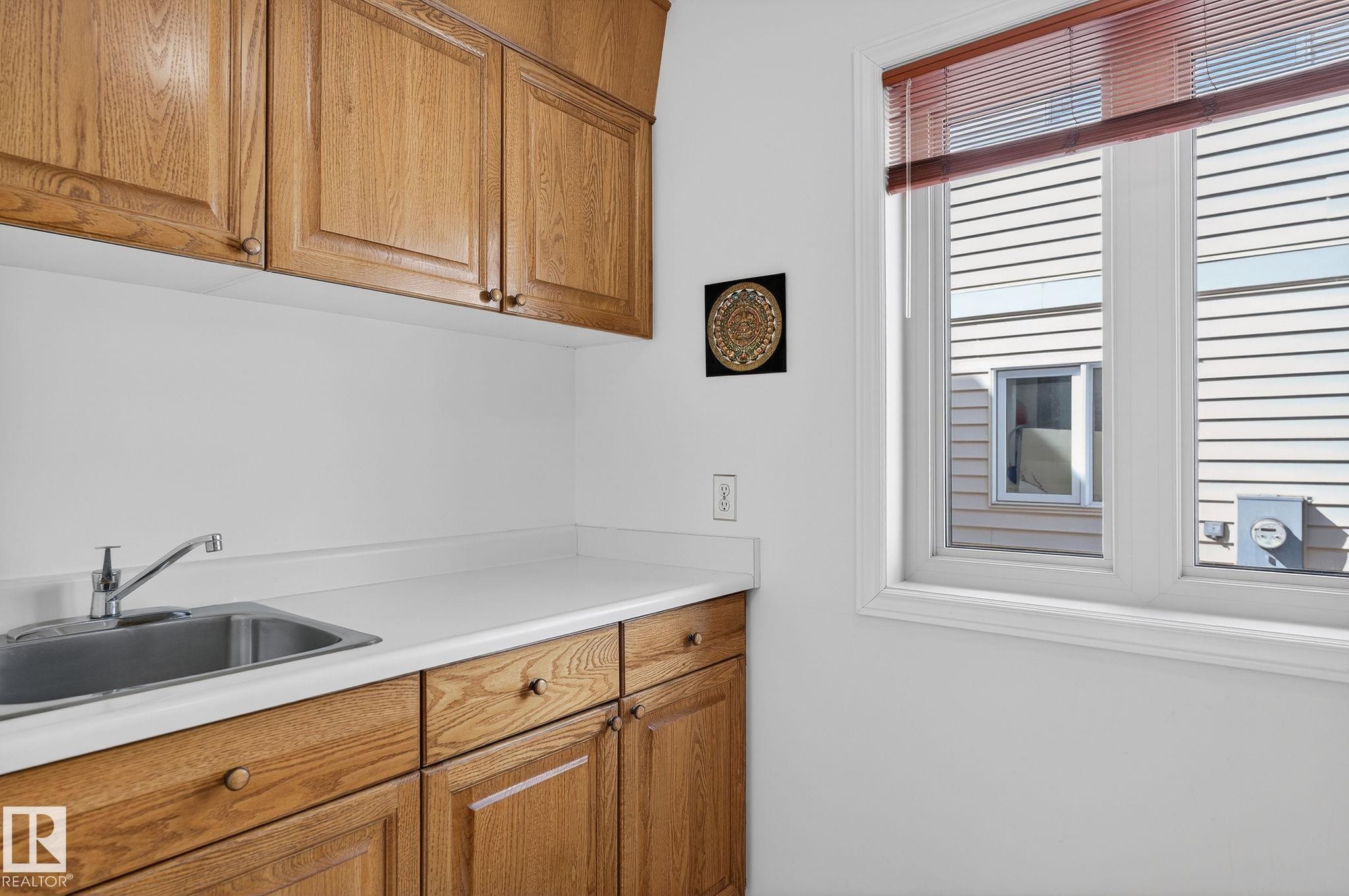Utility area featuring light wood-finish cabinetry, a stainless steel sink with a chrome faucet, and white countertops - 848 Wheeler Road W, Edmonton, AB - Indoor Photo Showing Kitchen