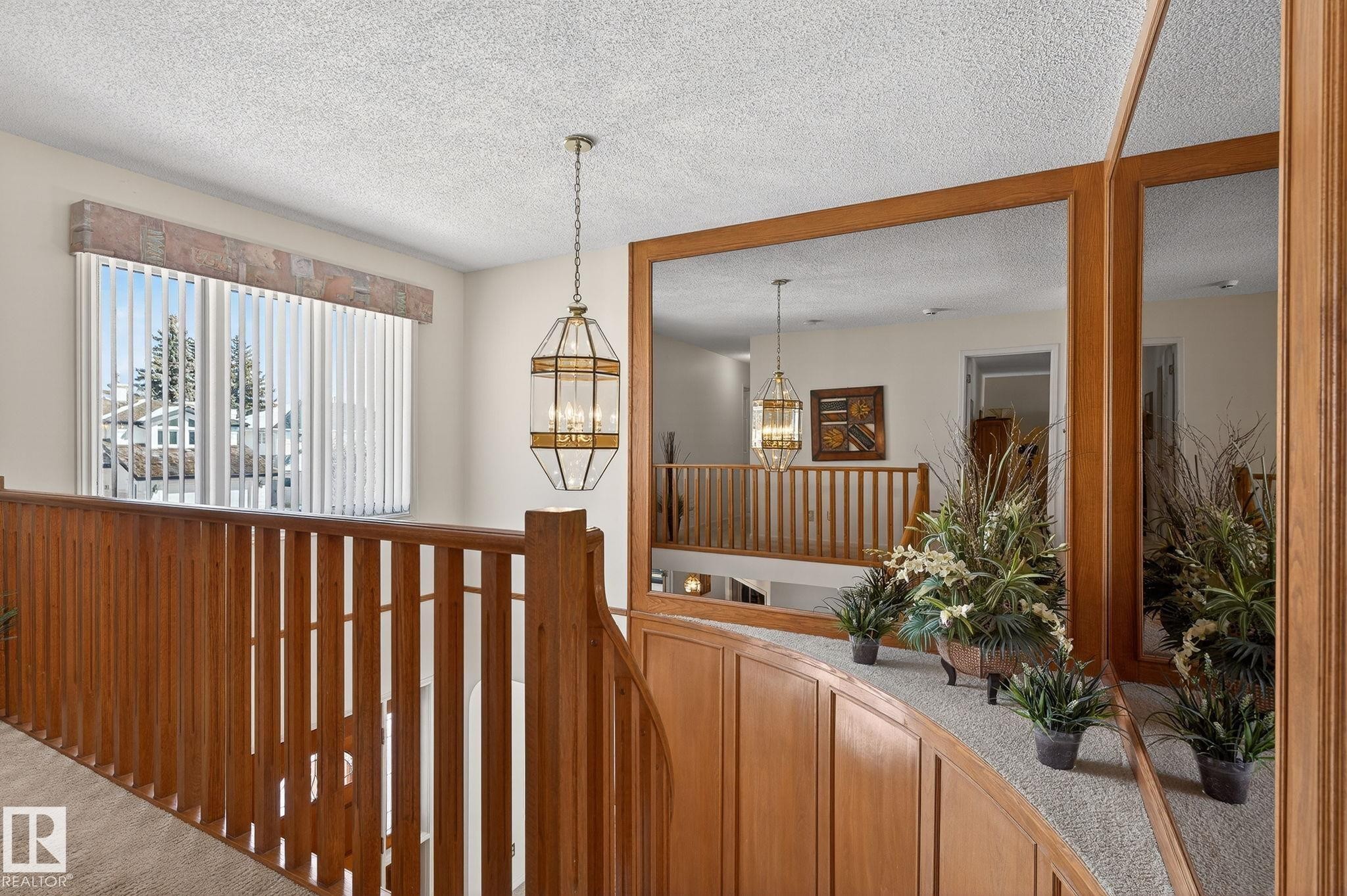 Hardwood railing and banister with a wood-paneled wall, overhead chandelier, and vertical blinds on a large window - 848 Wheeler Road W, Edmonton, AB - Indoor Photo Showing Other Room
