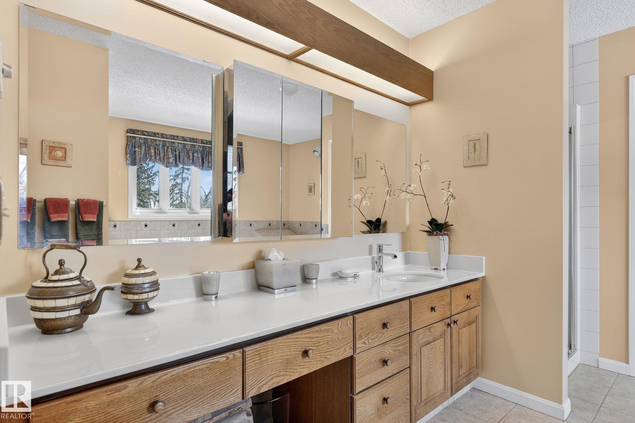 Bathroom vanity featuring wood cabinetry, white countertop, dual sinks with chrome fixtures, and mirrored medicine cabinets - 848 Wheeler Road W, Edmonton, AB - Indoor Photo Showing Bathroom