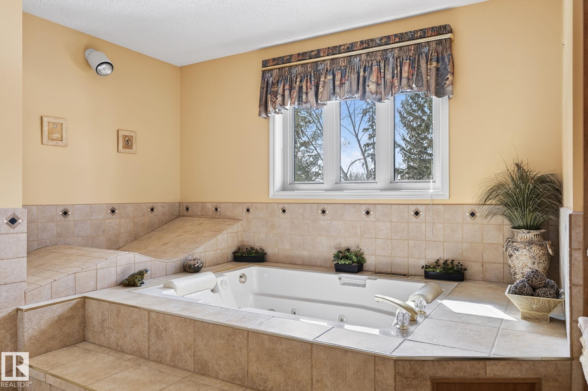 Integrated jetted tub set within a tiled surround, featuring a large window, tiled step-up entry, and a built-in tiled chaise - 848 Wheeler Road W, Edmonton, AB - Indoor Photo Showing Bathroom