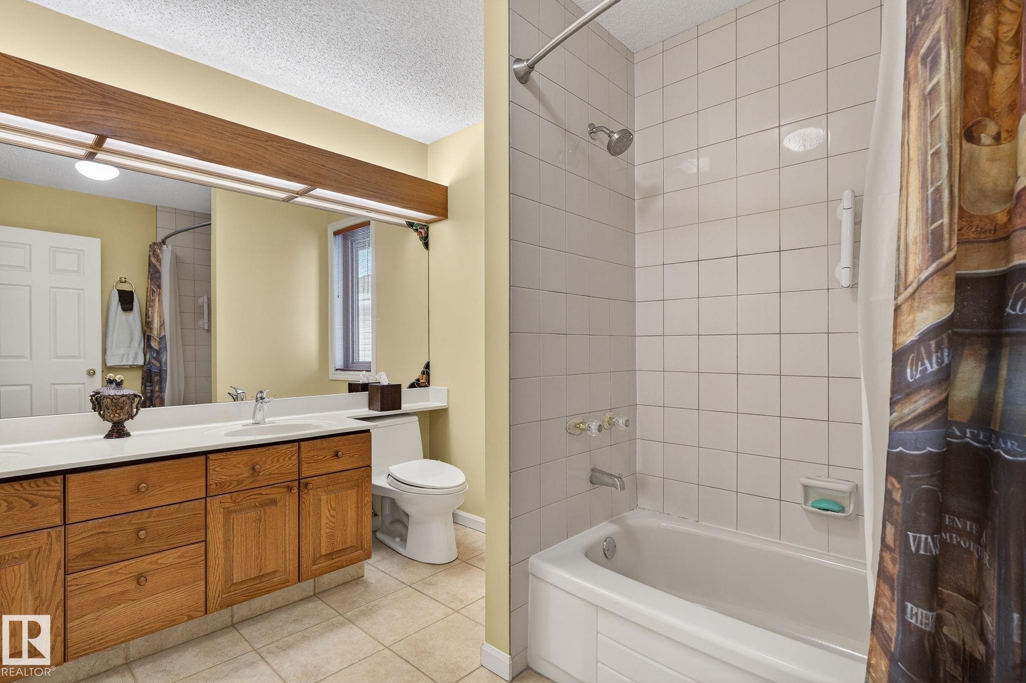 Bathroom featuring a light wood-finish vanity with a light-toned countertop, an integrated mirror with overhead lighting, a white toilet, and a bathtub with white subway tile surround - 848 Wheeler Road W, Edmonton, AB - Indoor Photo Showing Bathroom