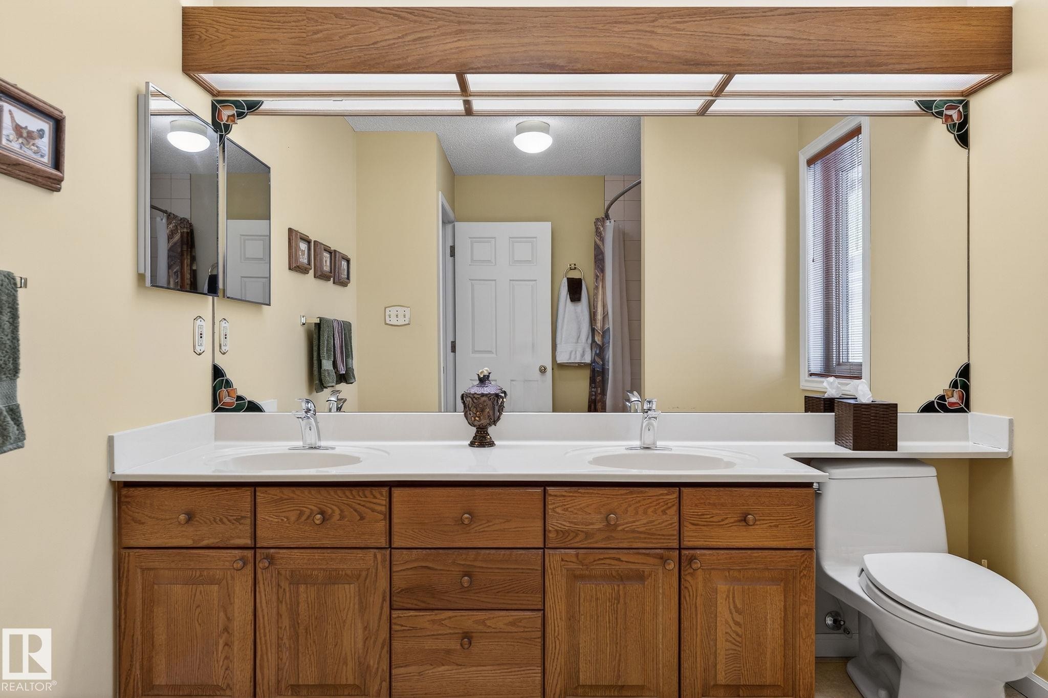Bathroom vanity featuring dual under-mount sinks, a white countertop, and wood-finish cabinetry with multiple storage drawers and doors - 848 Wheeler Road W, Edmonton, AB - Indoor Photo Showing Bathroom
