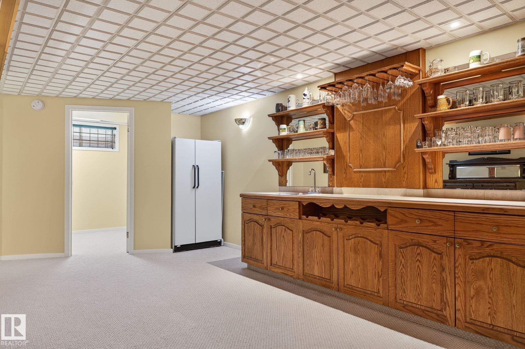 Recessed lighting illuminating a large oak-finish built-in wet bar with a stainless steel sink, under-mount wine storage, and an integrated beverage cooler - 848 Wheeler Road W, Edmonton, AB - Indoor