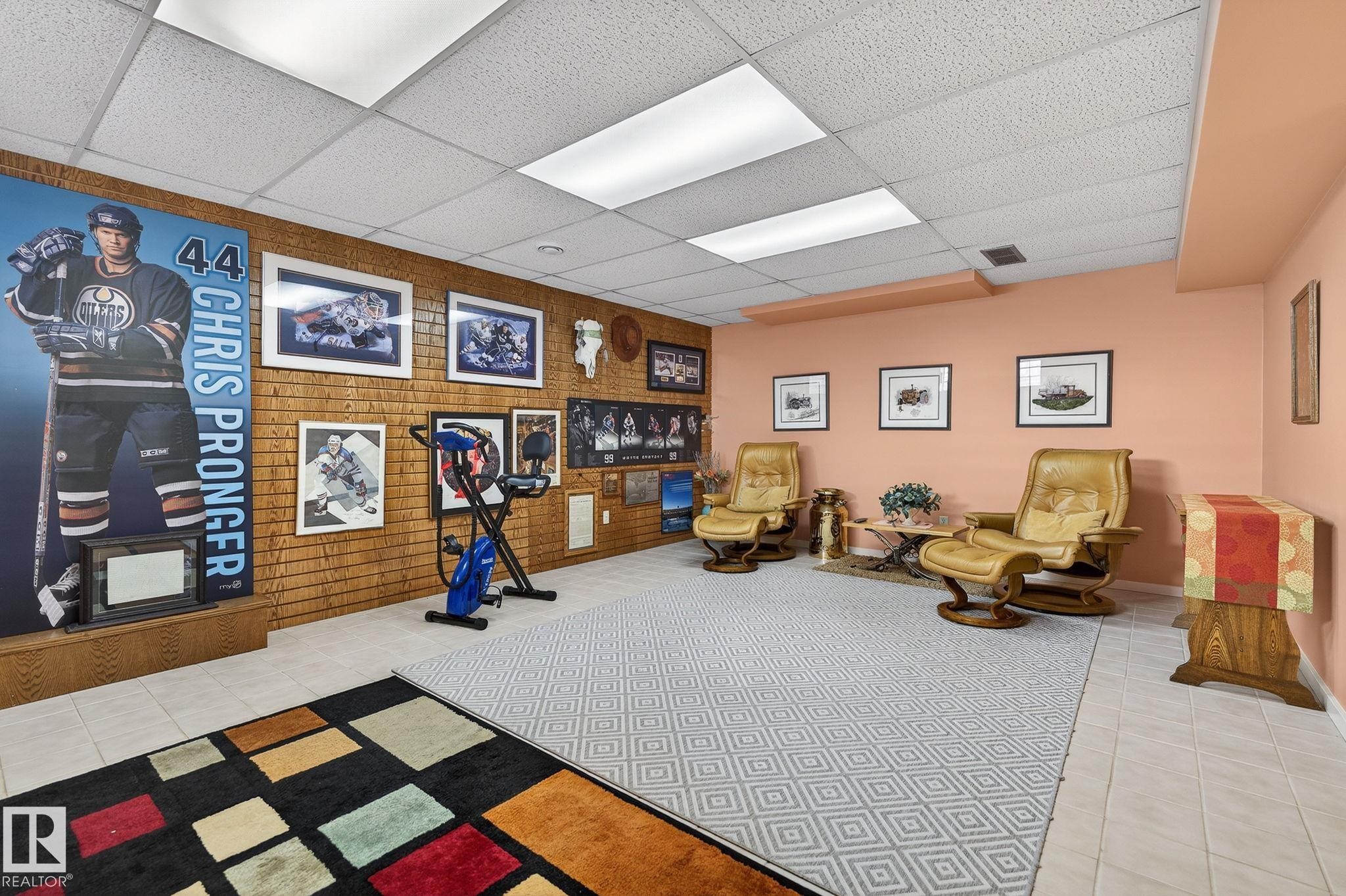 Spacious room featuring a drop-tile ceiling with integrated lighting, a textured brick accent wall, light-toned wall paint, and tile flooring - 848 Wheeler Road W, Edmonton, AB - Indoor