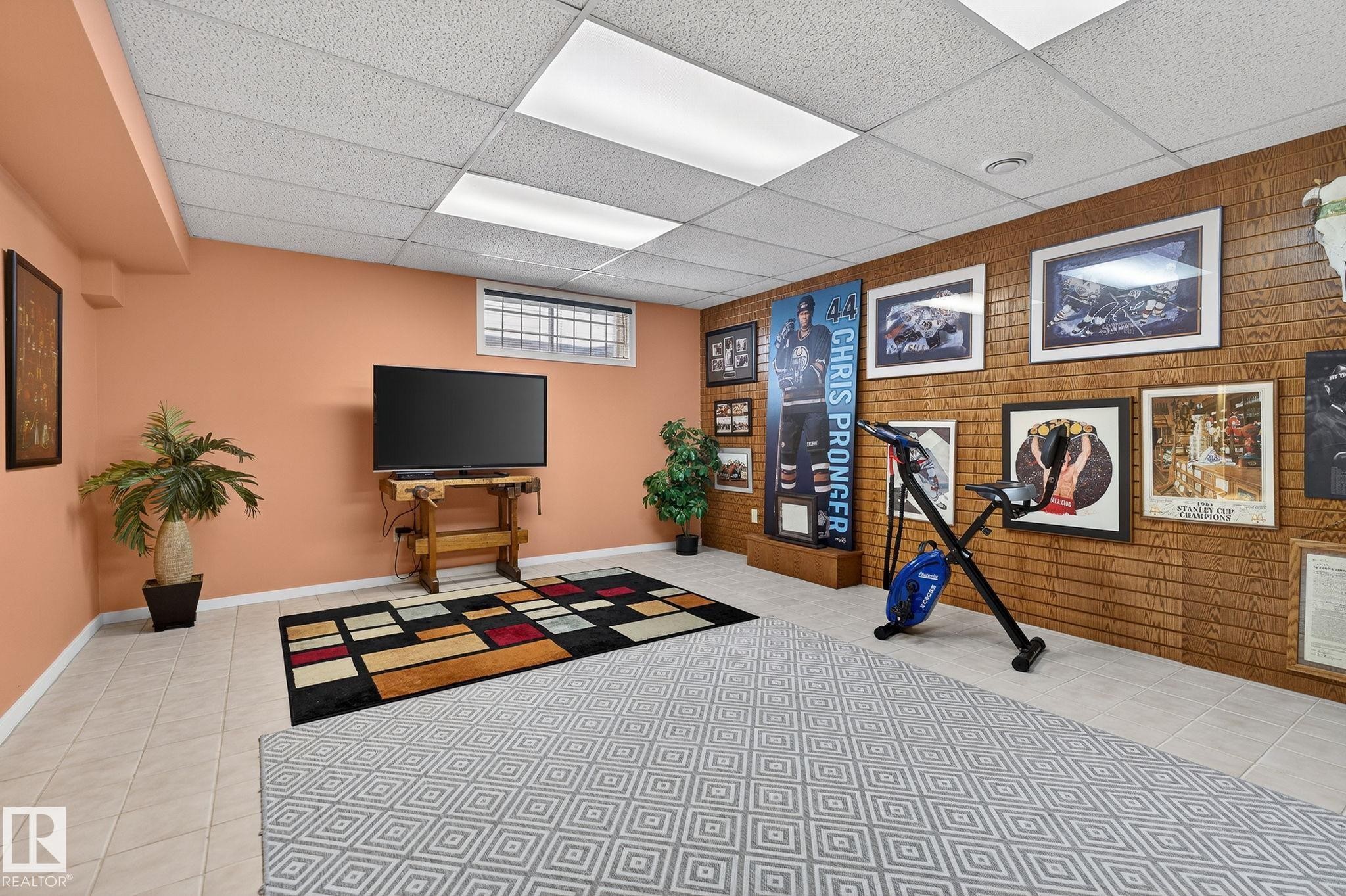 Spacious room featuring tile flooring, a drop ceiling with integrated lighting, and a window with security bars - 848 Wheeler Road W, Edmonton, AB - Indoor Photo Showing Other Room