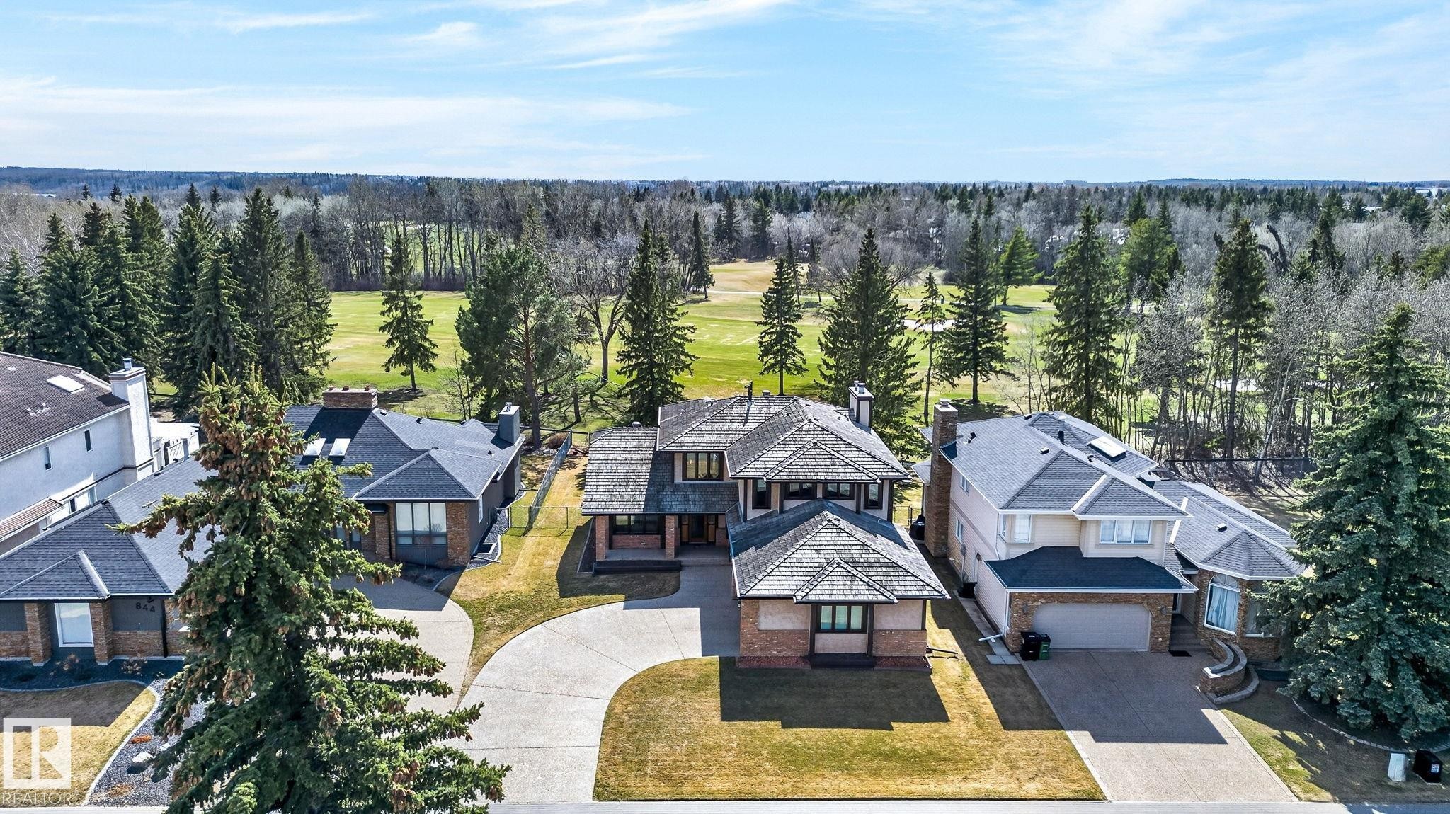 Expansive property featuring a multi-story residence with a paved driveway, mature trees, and a green space backdrop - 848 Wheeler Road W, Edmonton, AB - Outdoor With Facade