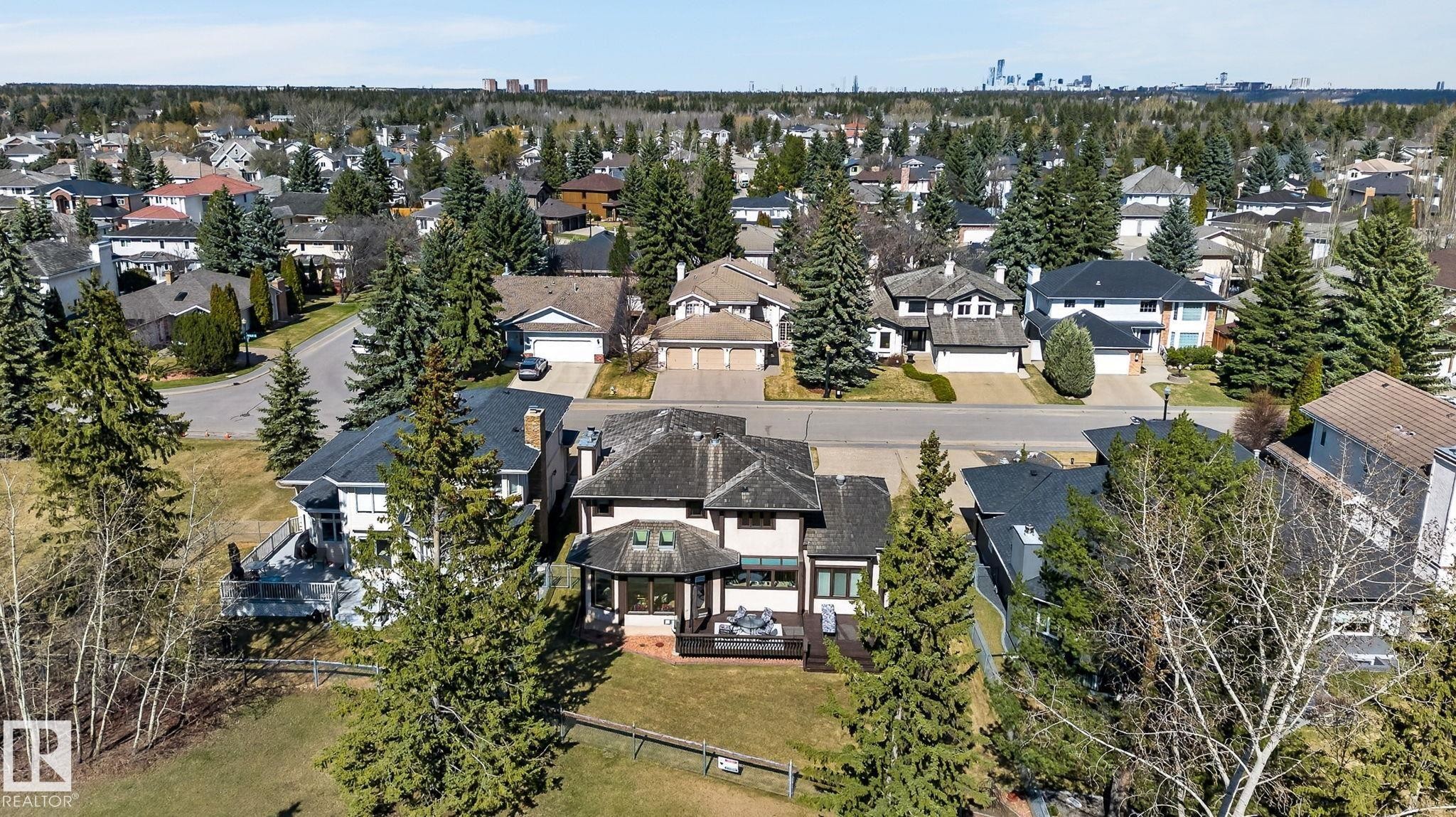 Contemporary residence featuring a dark shingled roof, a spacious rear deck, and mature evergreen trees - 848 Wheeler Road W, Edmonton, AB - Outdoor With View